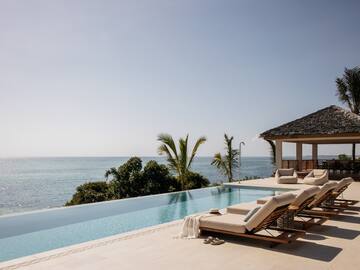a pool with lounge chairs and a gazebo overlooking the ocean