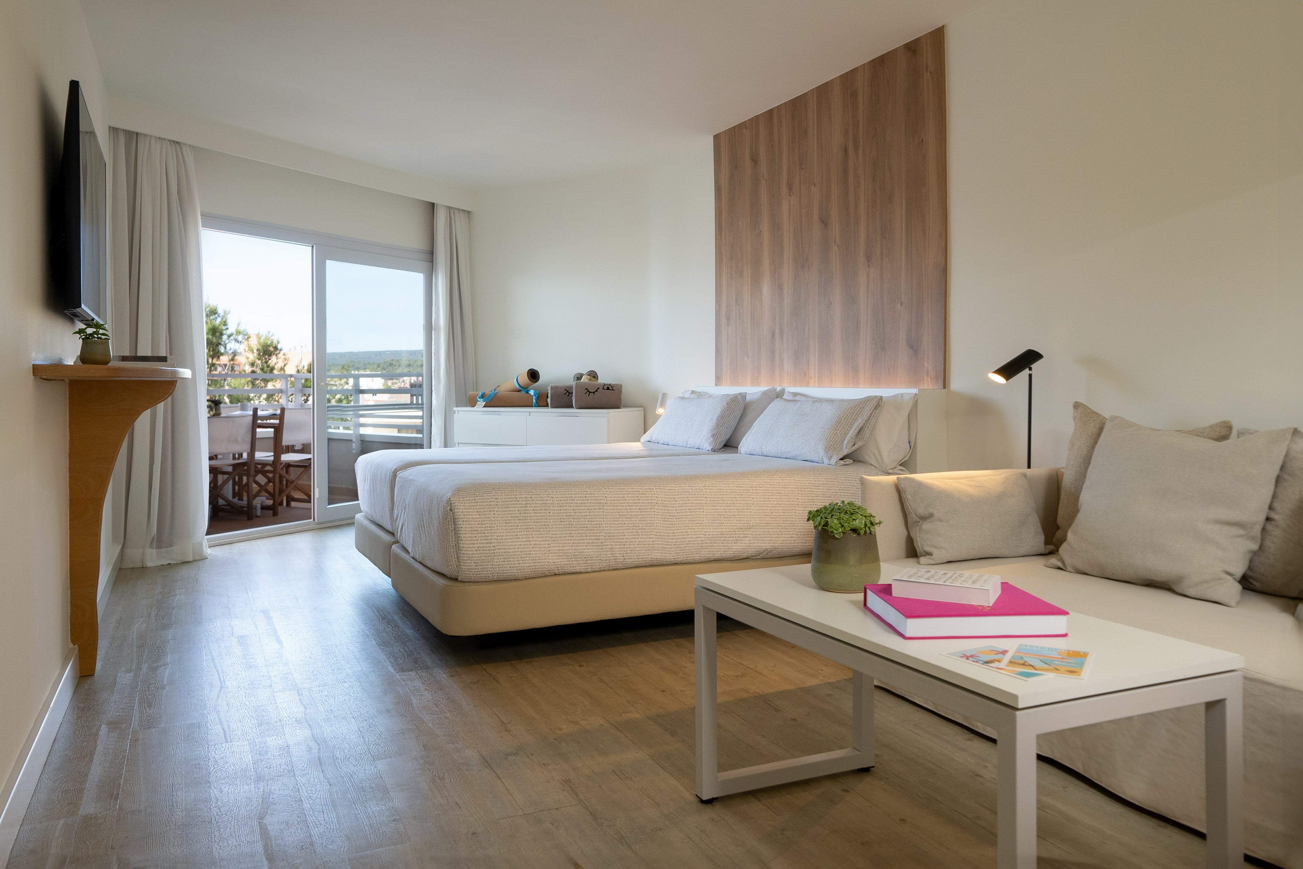 Bright modern hotel room with twin beds, sofa seating, and balcony access.