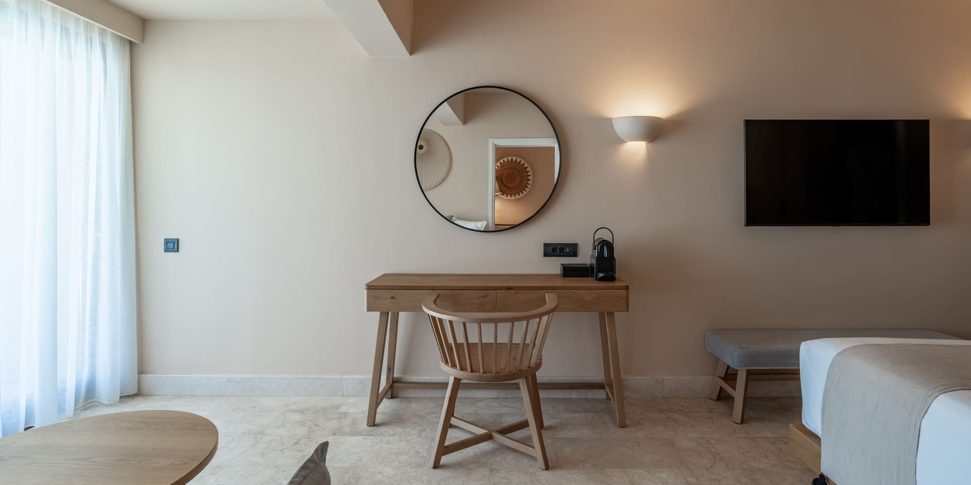 Modern hotel room with wooden desk, round mirror, and TV.