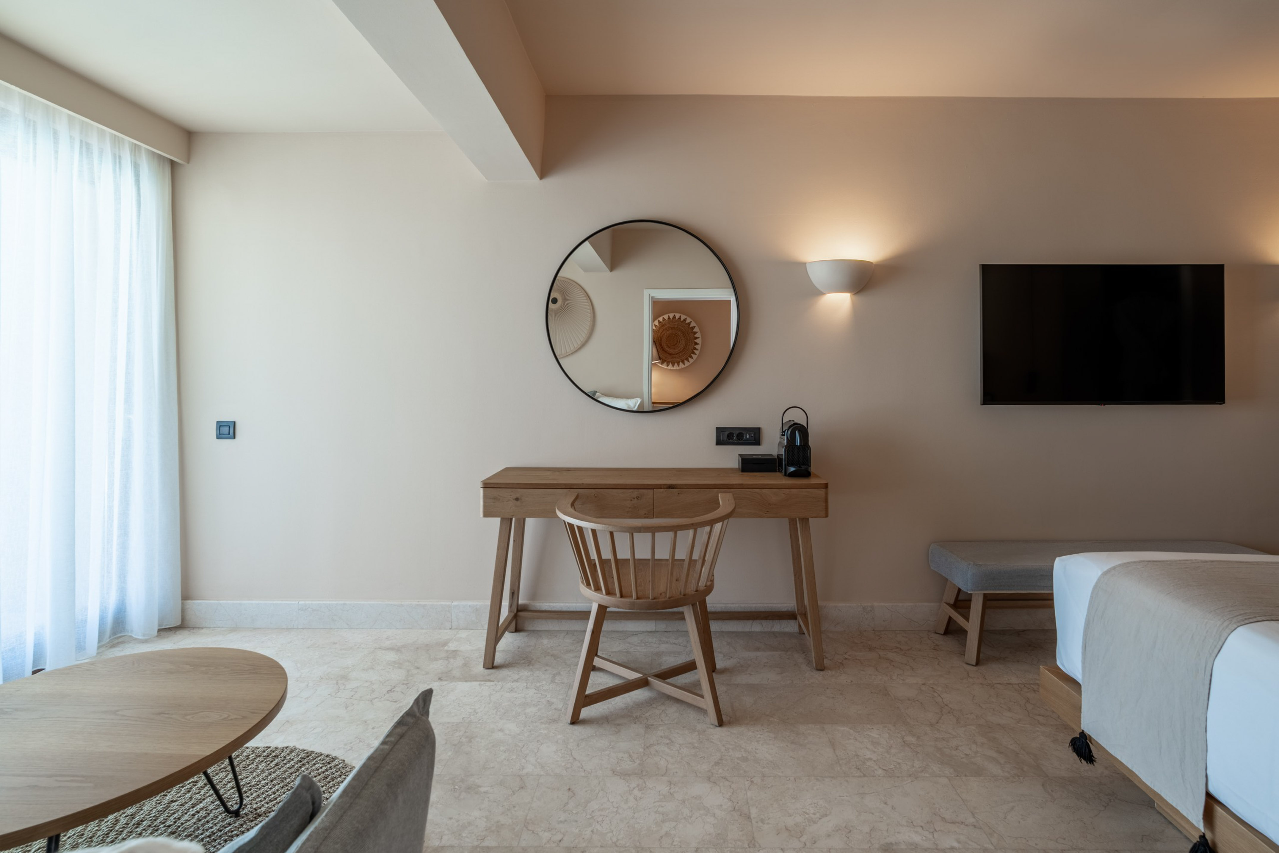 Modern hotel room with wooden desk, round mirror, and TV.
