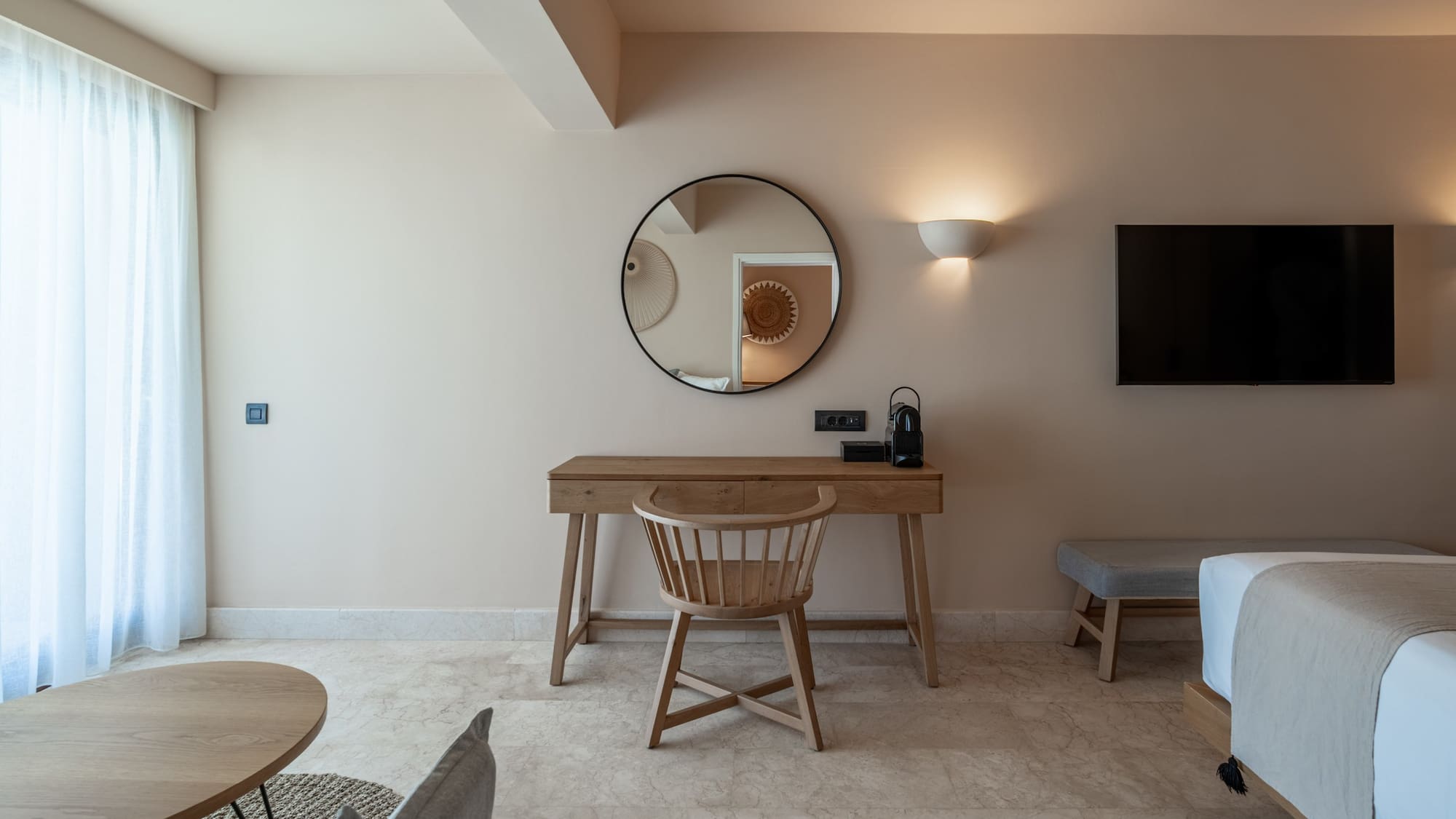 Modern hotel room with wooden desk, round mirror, and TV.