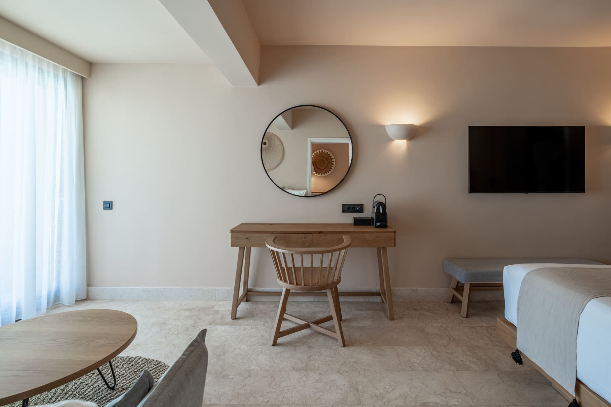 Modern hotel room with wooden desk, round mirror, and TV.
