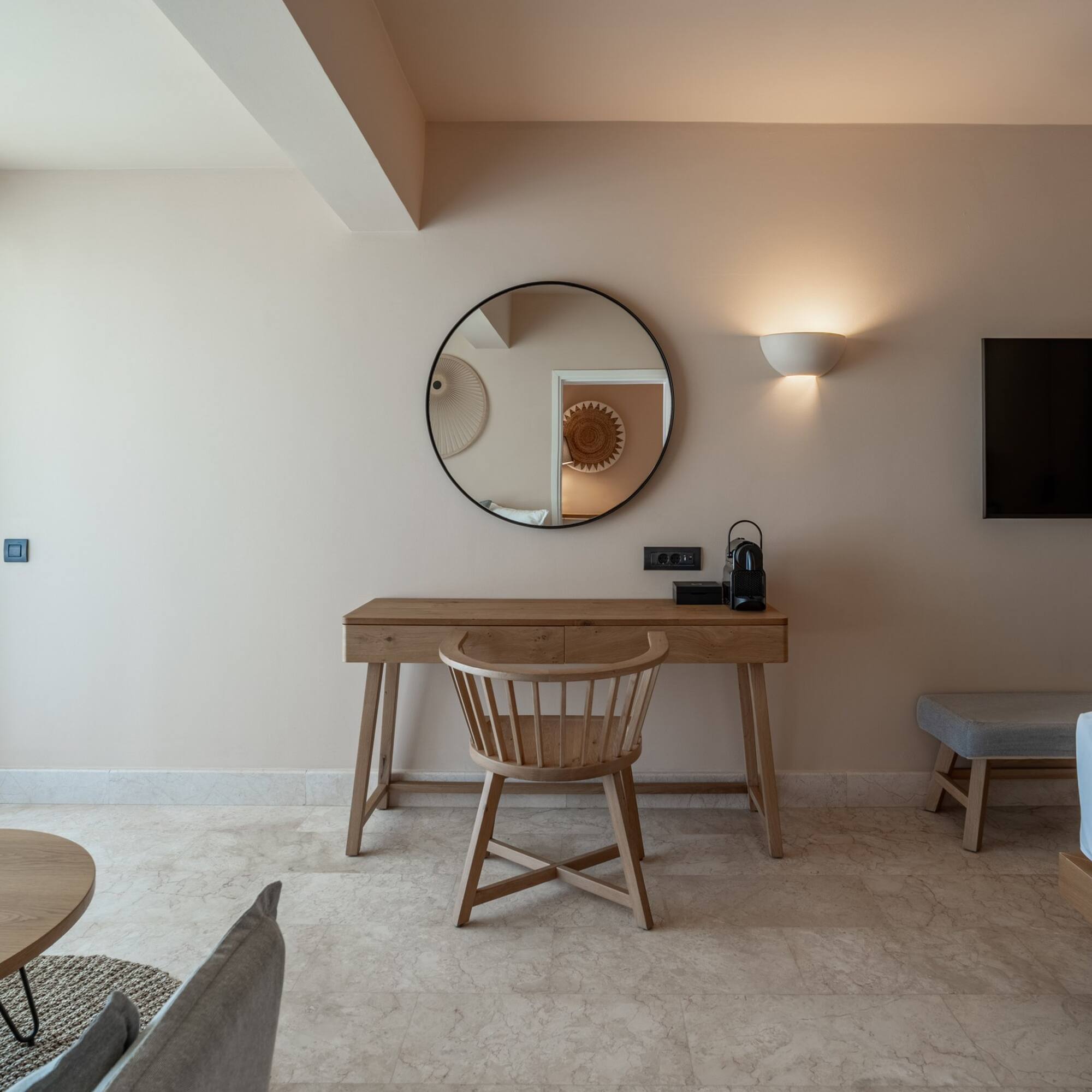 Modern hotel room with wooden desk, round mirror, and TV.