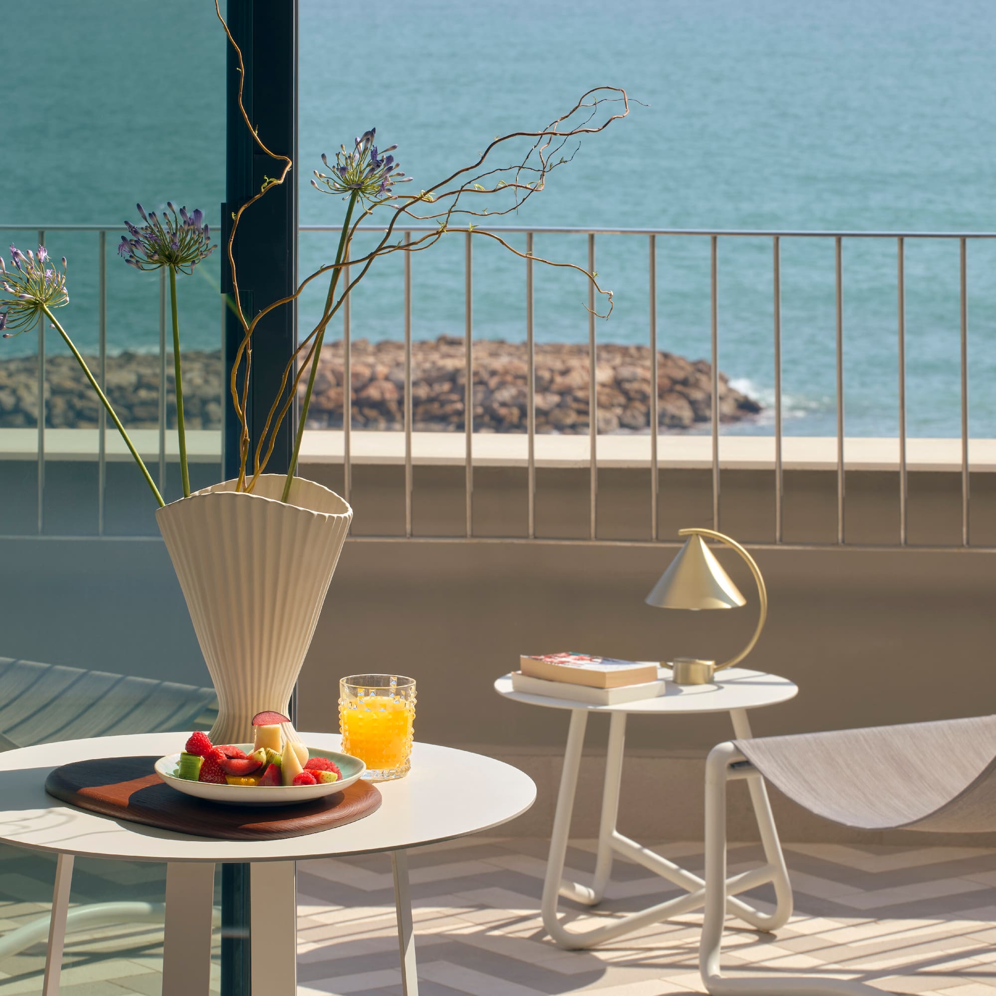 a table with fruit and a vase on it on a balcony overlooking water