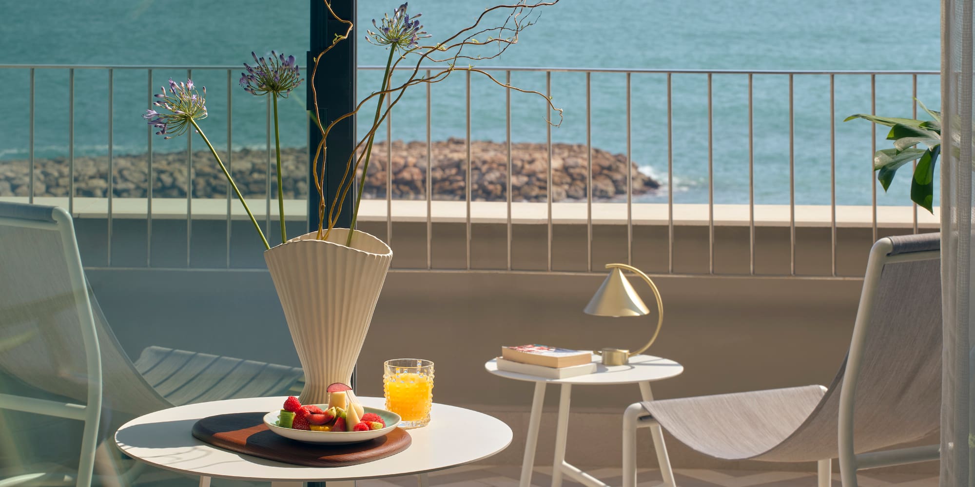 a table with fruit and a vase on it on a balcony overlooking water