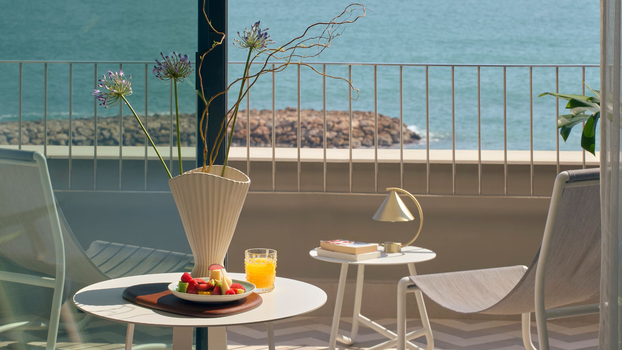 a table with fruit and a vase on it on a balcony overlooking water