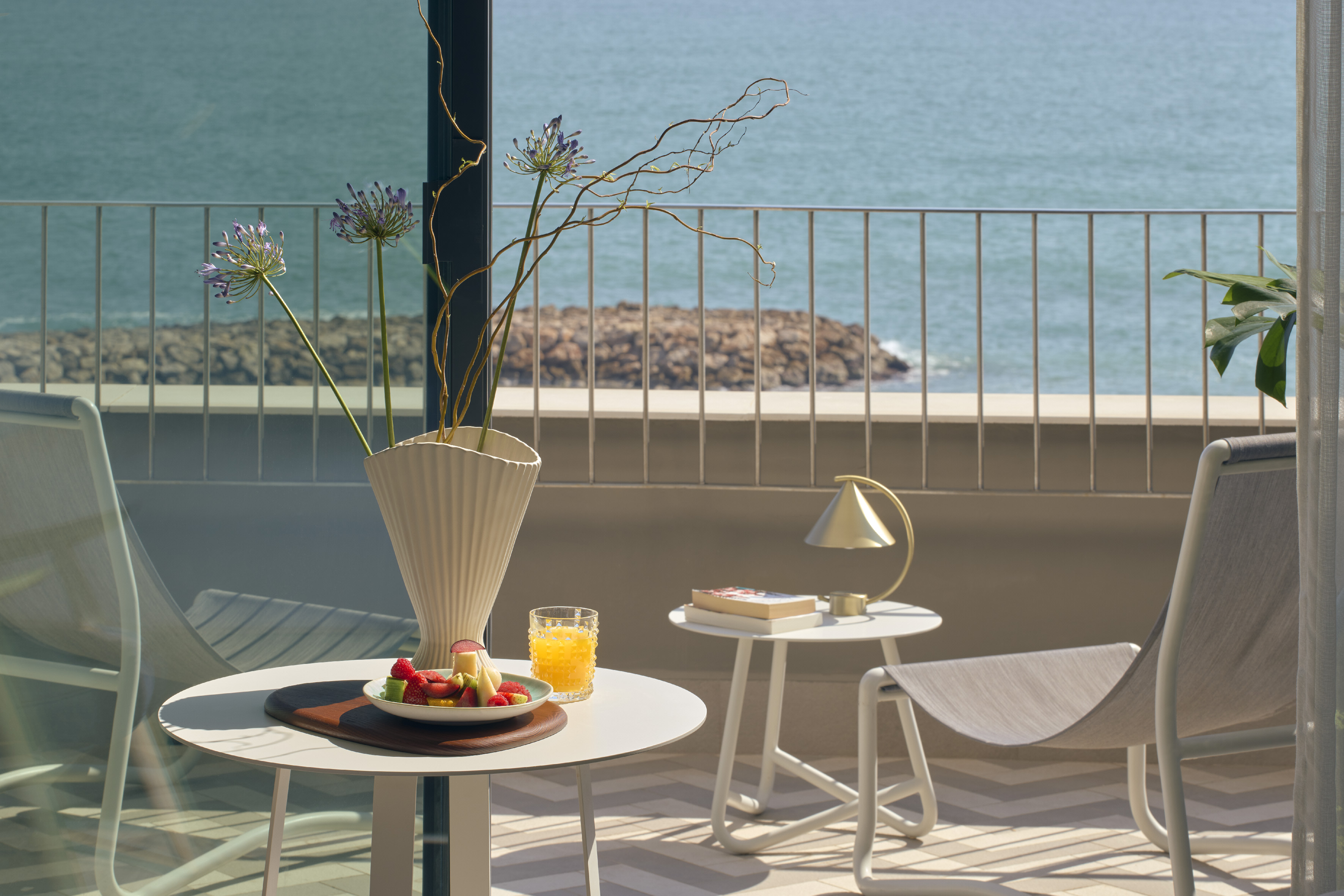 Balcony with sea view, fruit breakfast, juice, flowers, and outdoor seating.