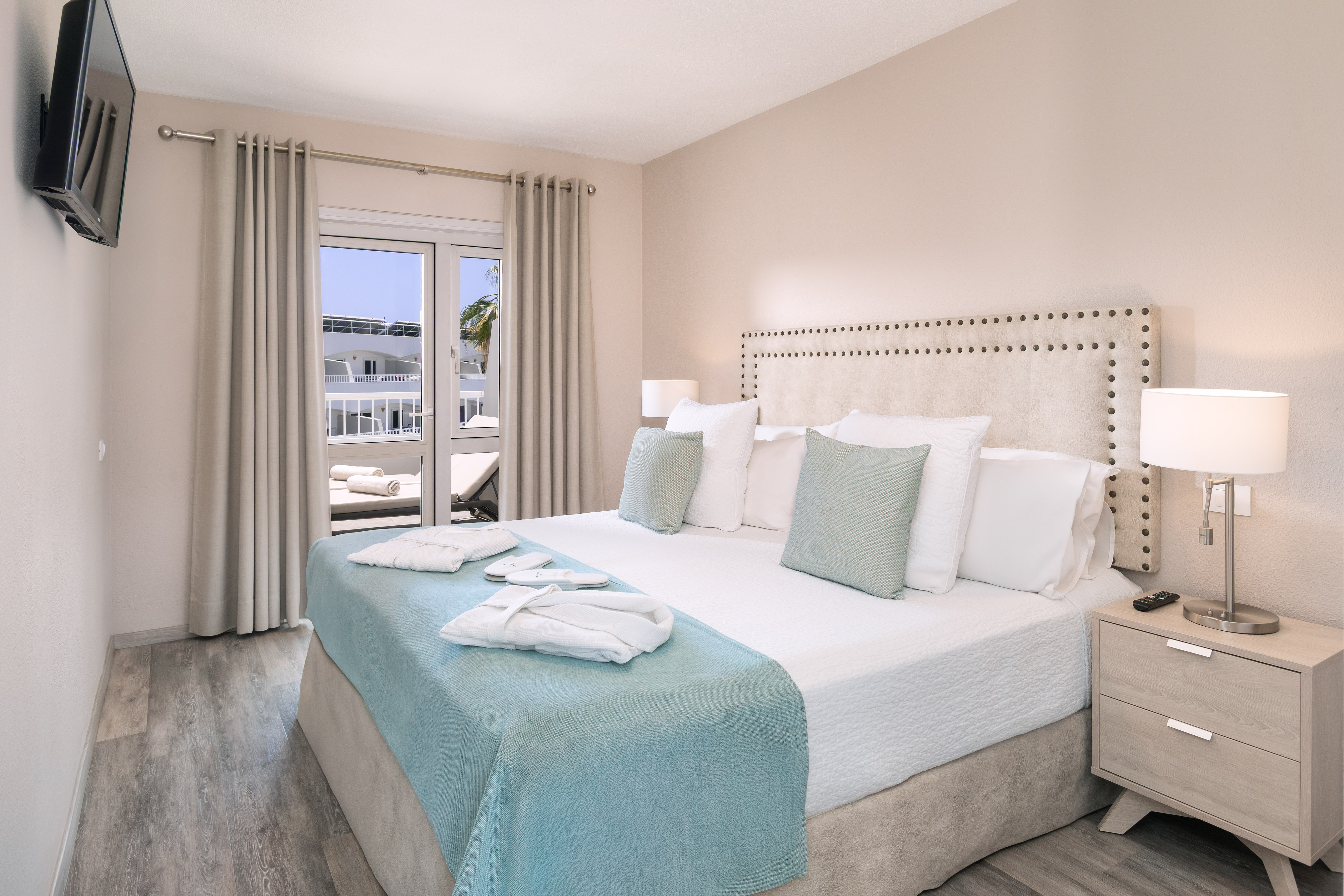 Bright hotel bedroom with large bed, balcony view, and modern light decor.