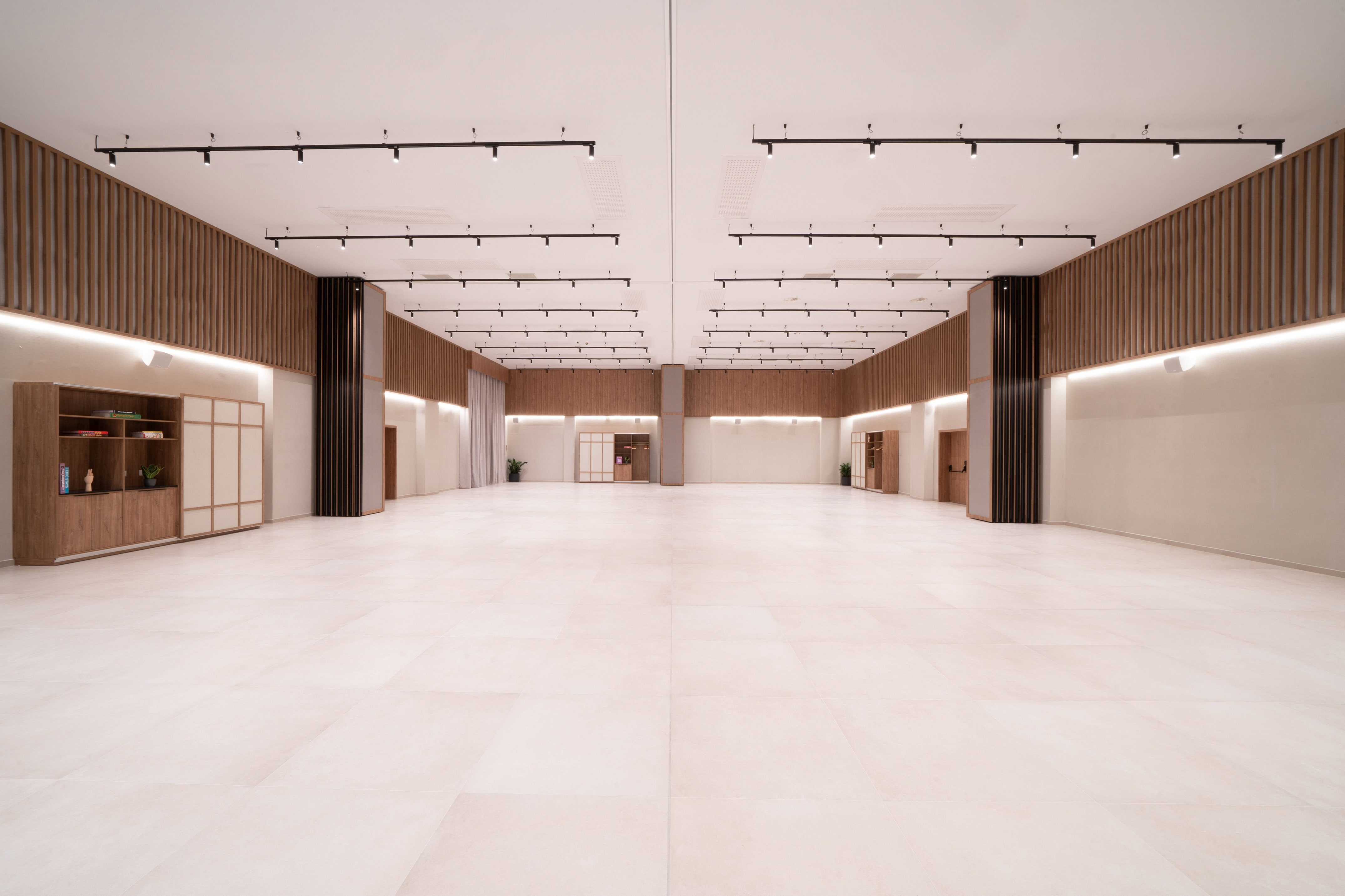 Modern empty event hall with wood paneling, track lighting, and light tiled floor.