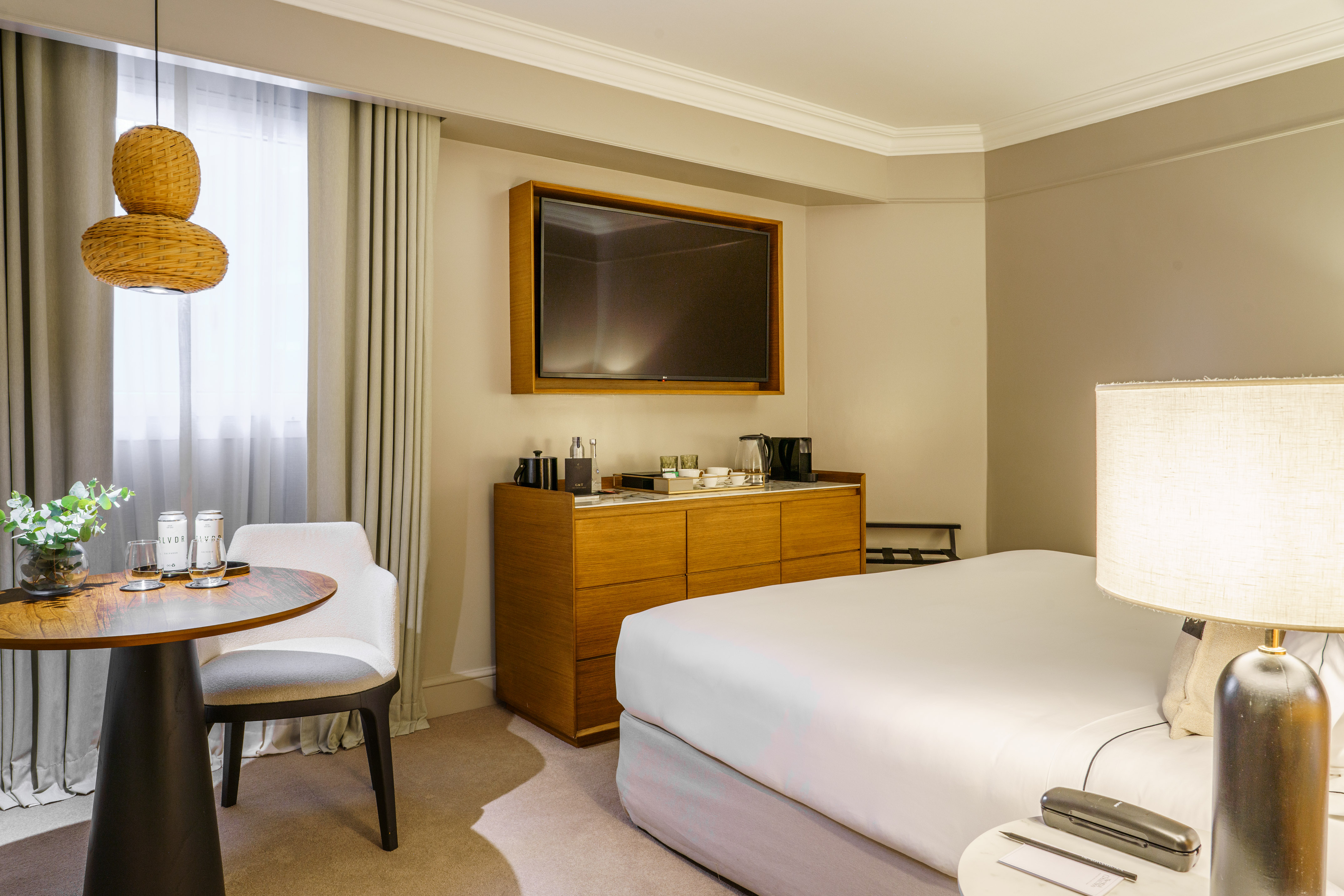 Modern hotel room with queen bed, mounted TV, wooden console, and small table.