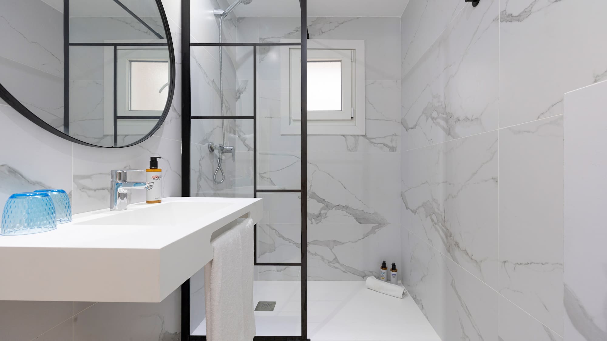 Modern white marble bathroom with black framed glass shower and floating vanity.