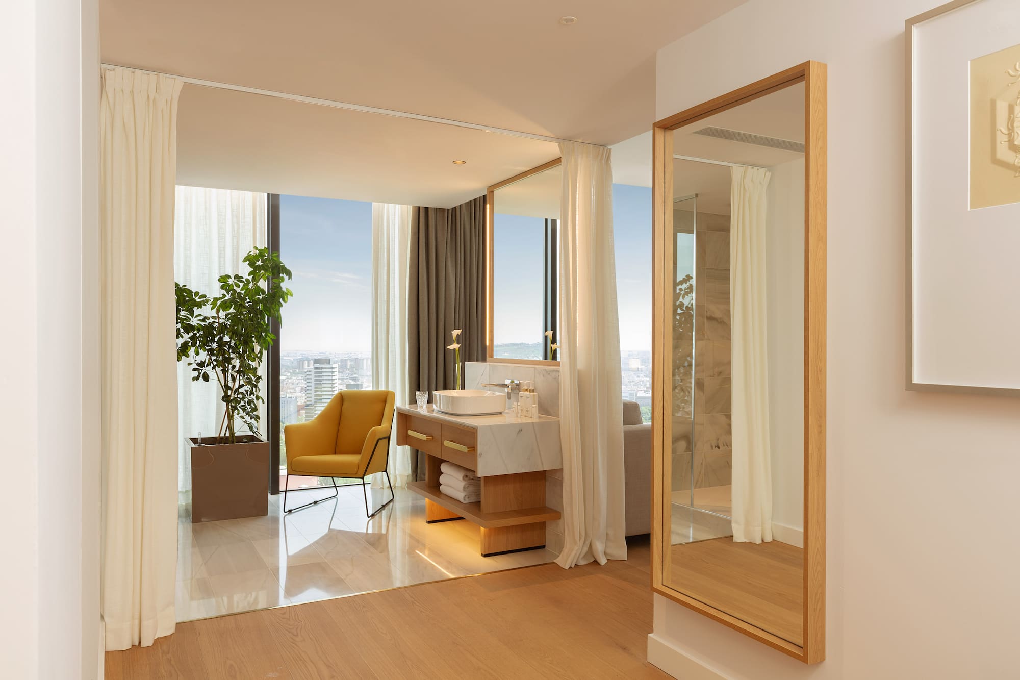 Luxury hotel suite with modern bathroom vanity, city view, and yellow armchair.