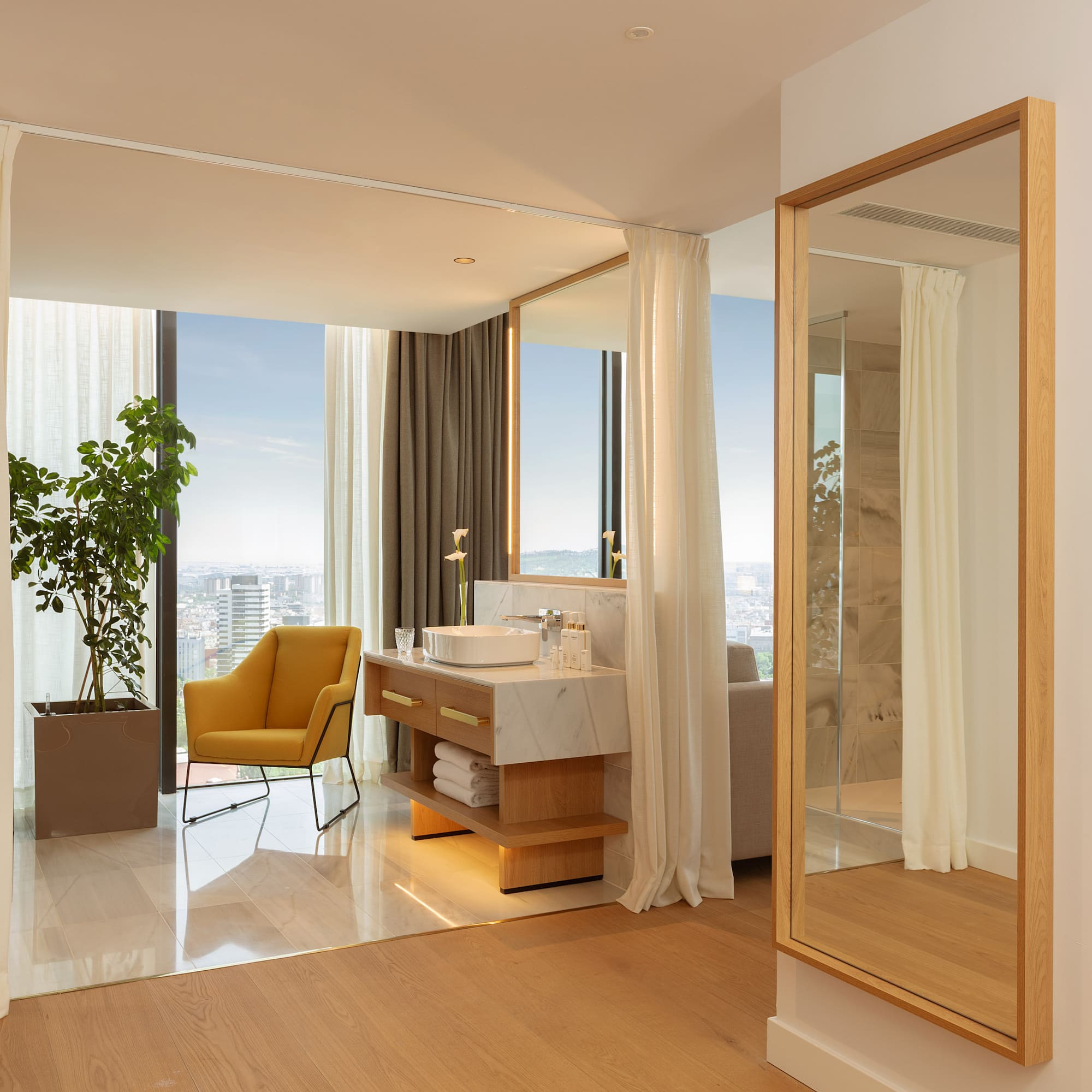 Luxury hotel suite with modern bathroom vanity, city view, and yellow armchair.