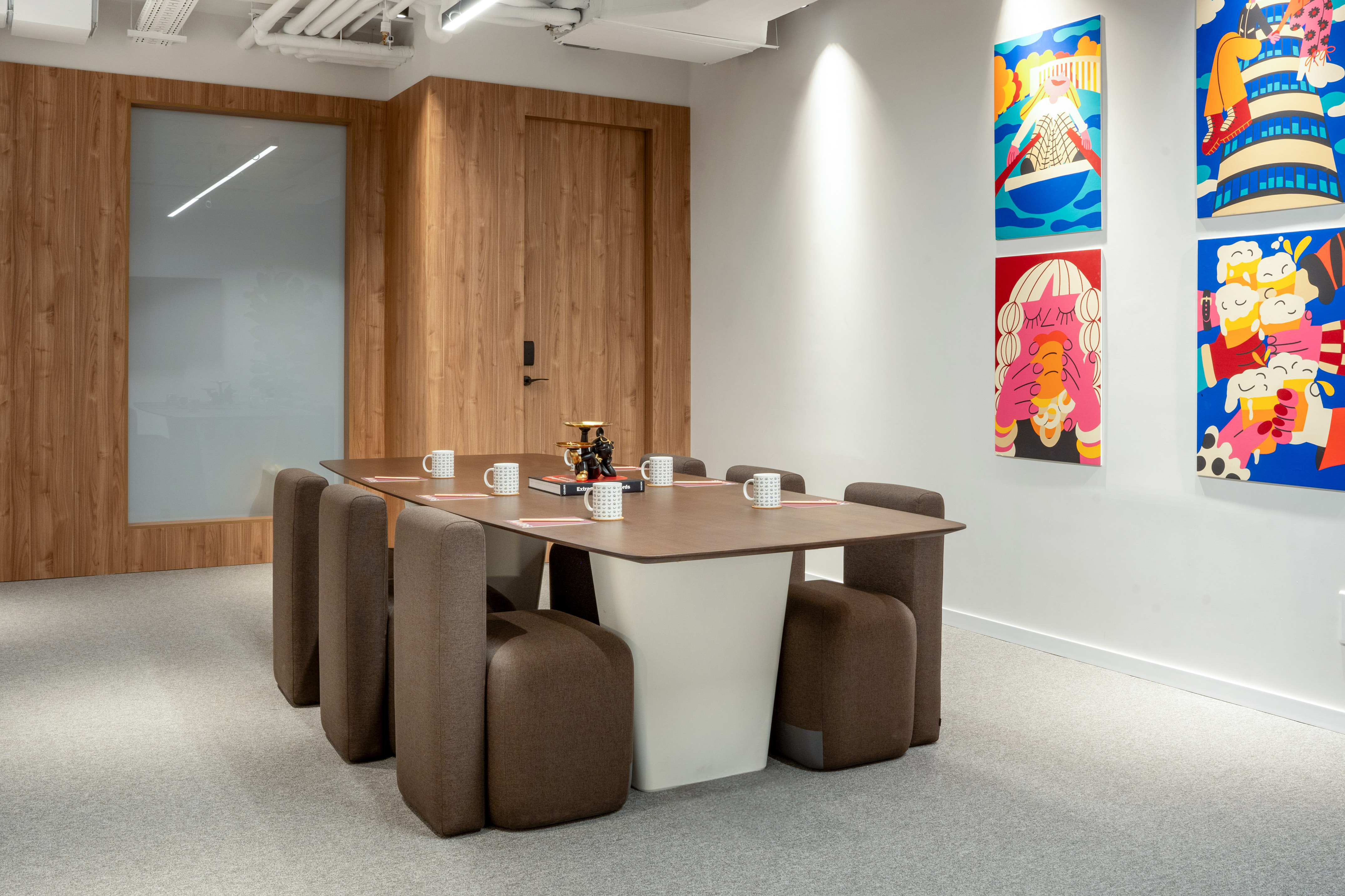 Modern conference room with brown table, 8 chairs, wood paneling, colorful art.