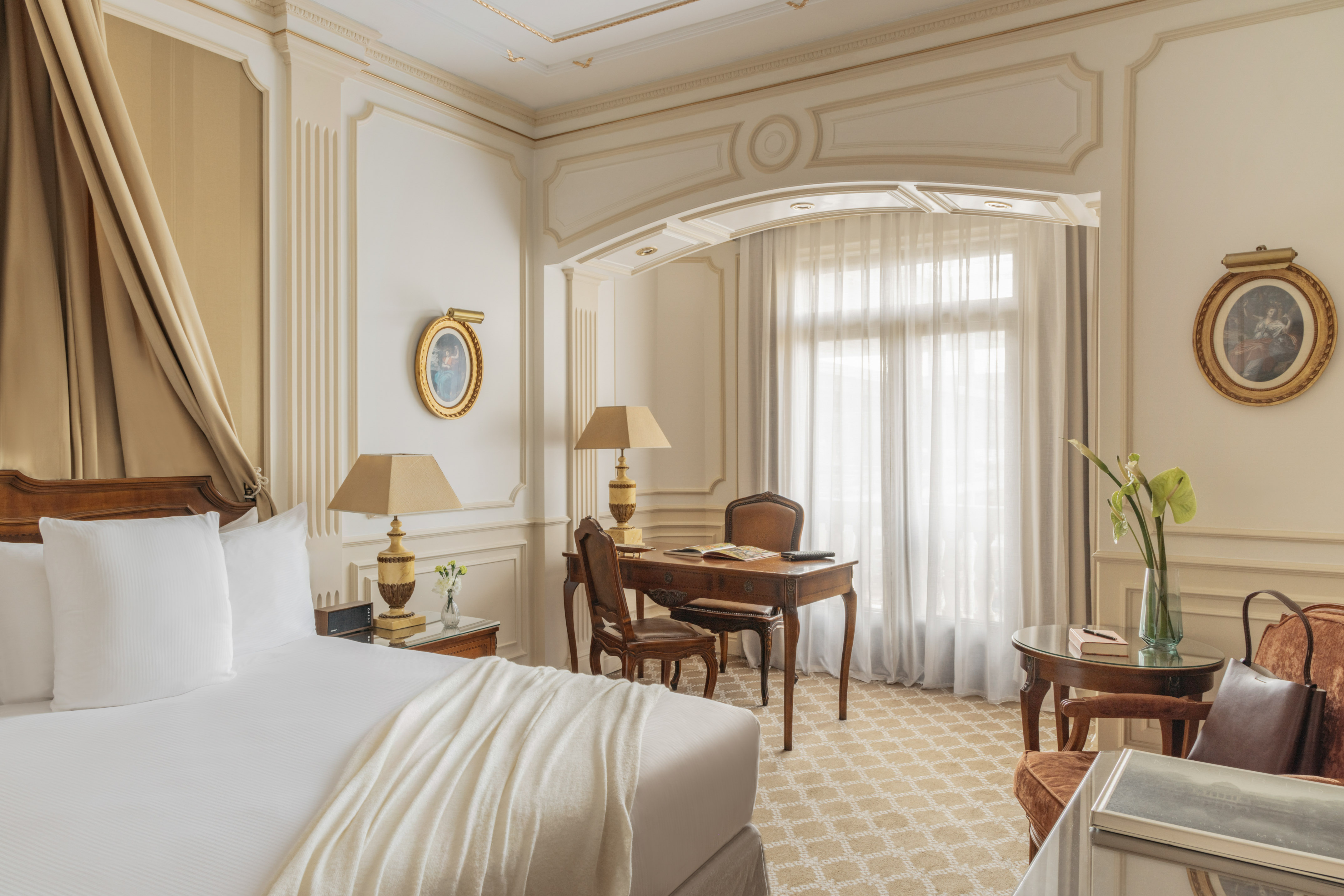 Luxury hotel suite with elegant white bed, classic desk, and ornate wall decor.