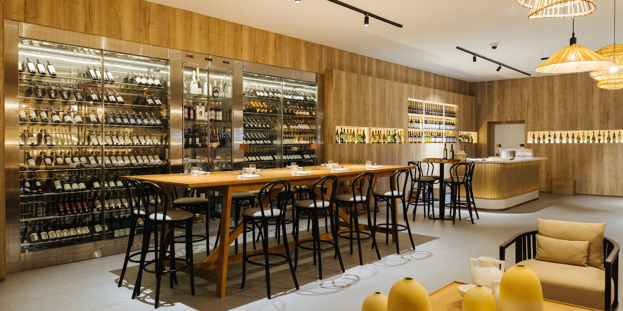 Modern wine bar interior with long tasting table and large wine cellar display.