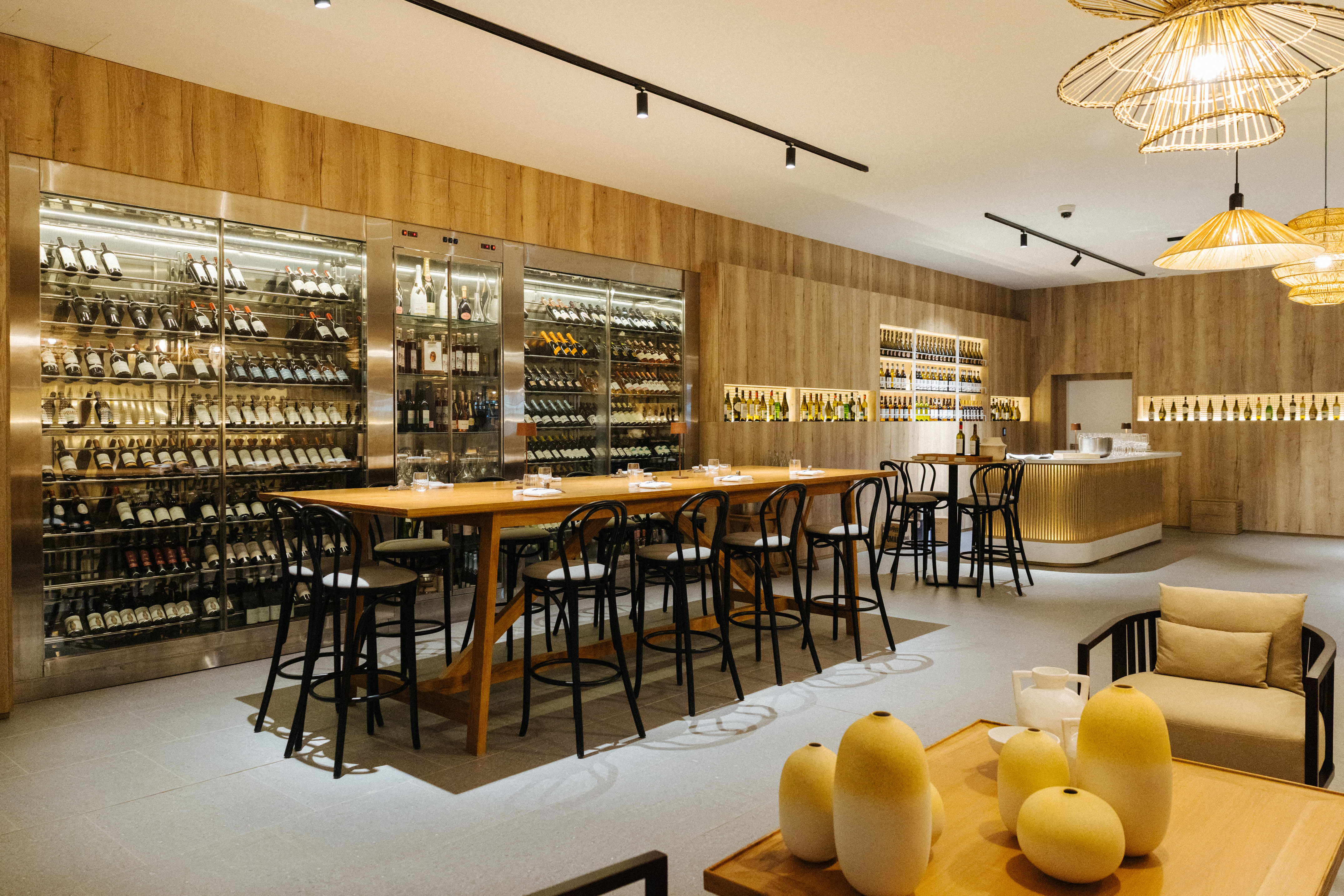 Modern wine bar interior with long tasting table and large wine cellar display.