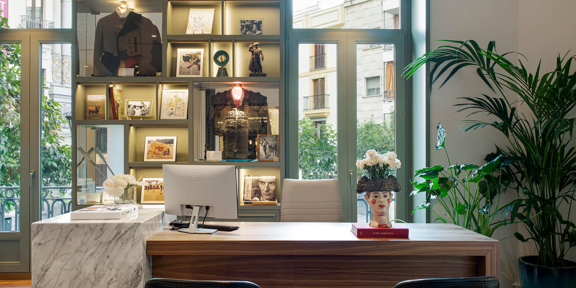 a desk with a computer and a display case in front of a window