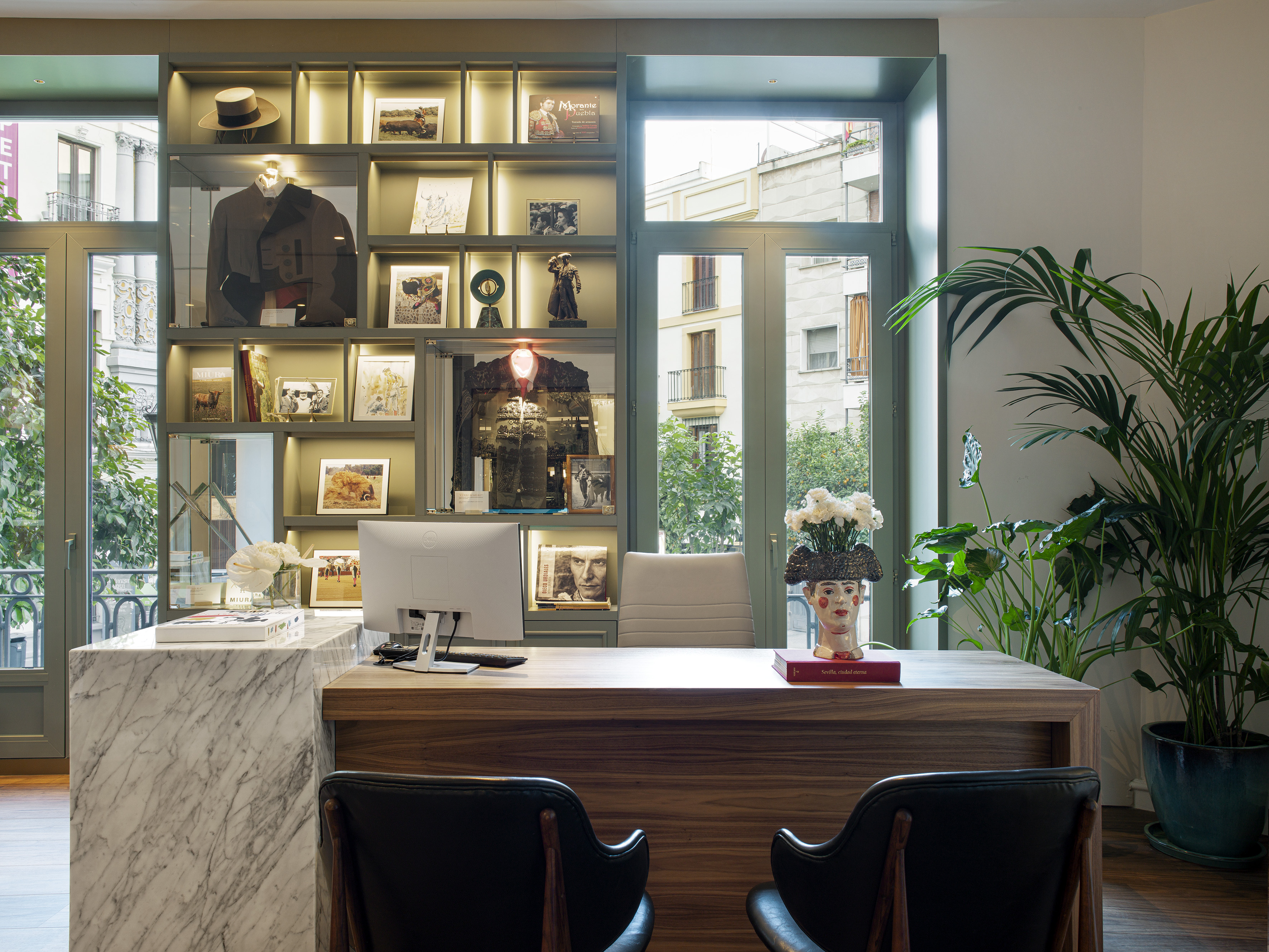 a desk with a computer and a display case in front of a window
