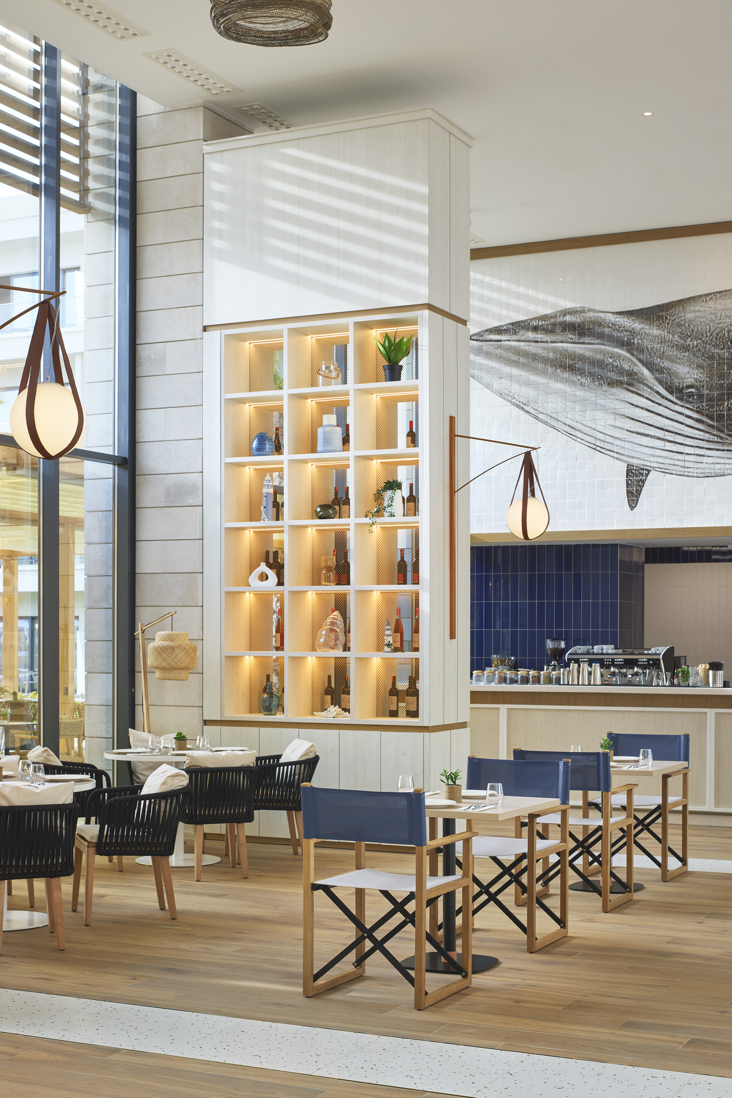 Modern restaurant dining room with whale mural, illuminated shelving, and cafe bar.