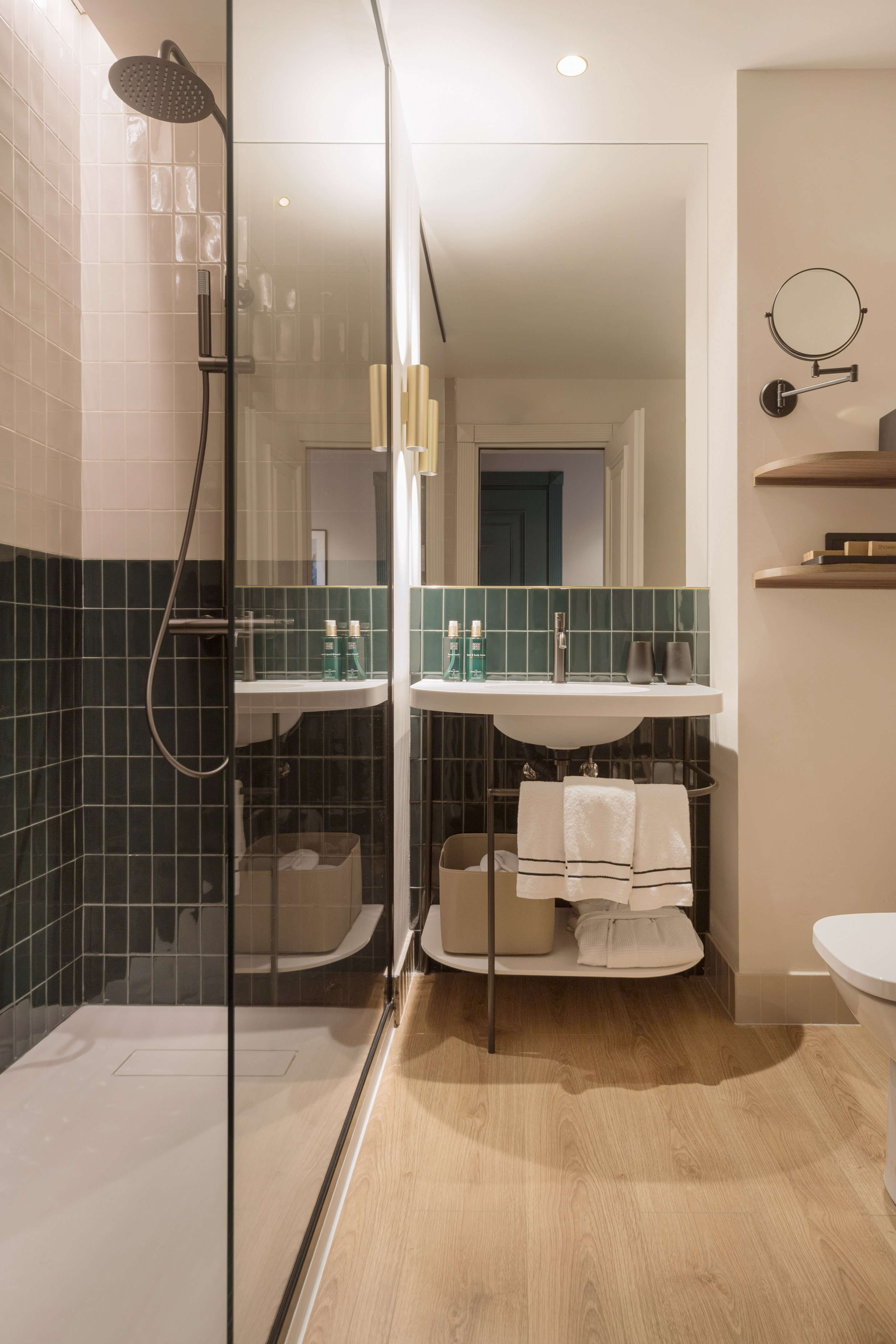 Modern bathroom with glass shower, dark green tile walls, vanity, and wood floor.