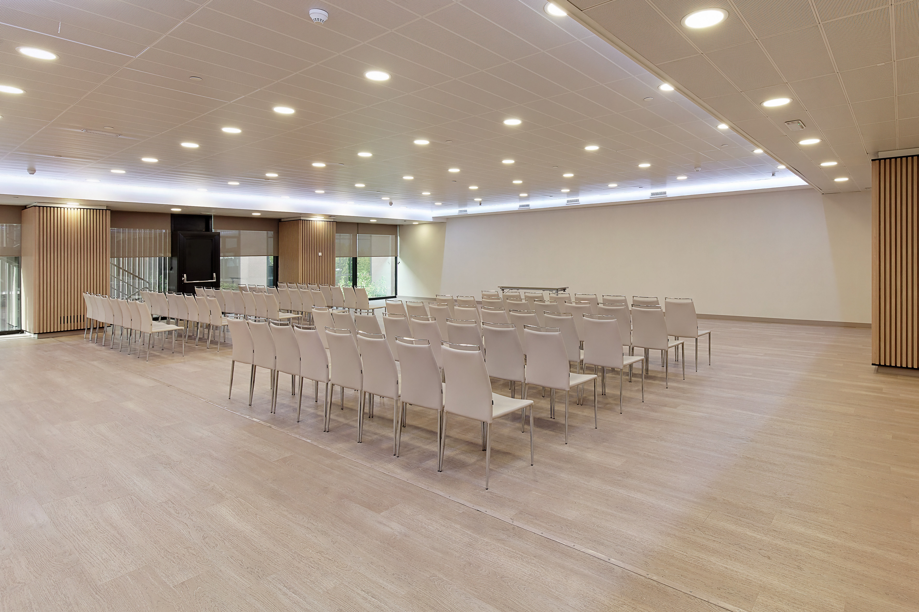 Modern conference room with rows of white chairs and light wood floor.
