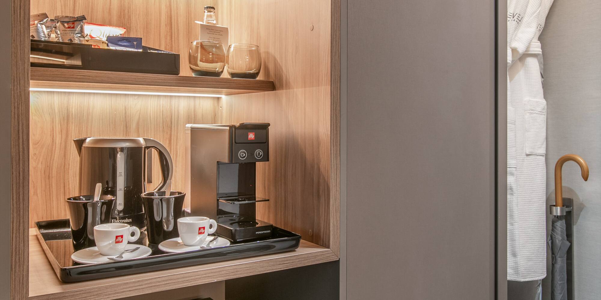 Modern hotel minibar, coffee station, and closet with illuminated shelves.