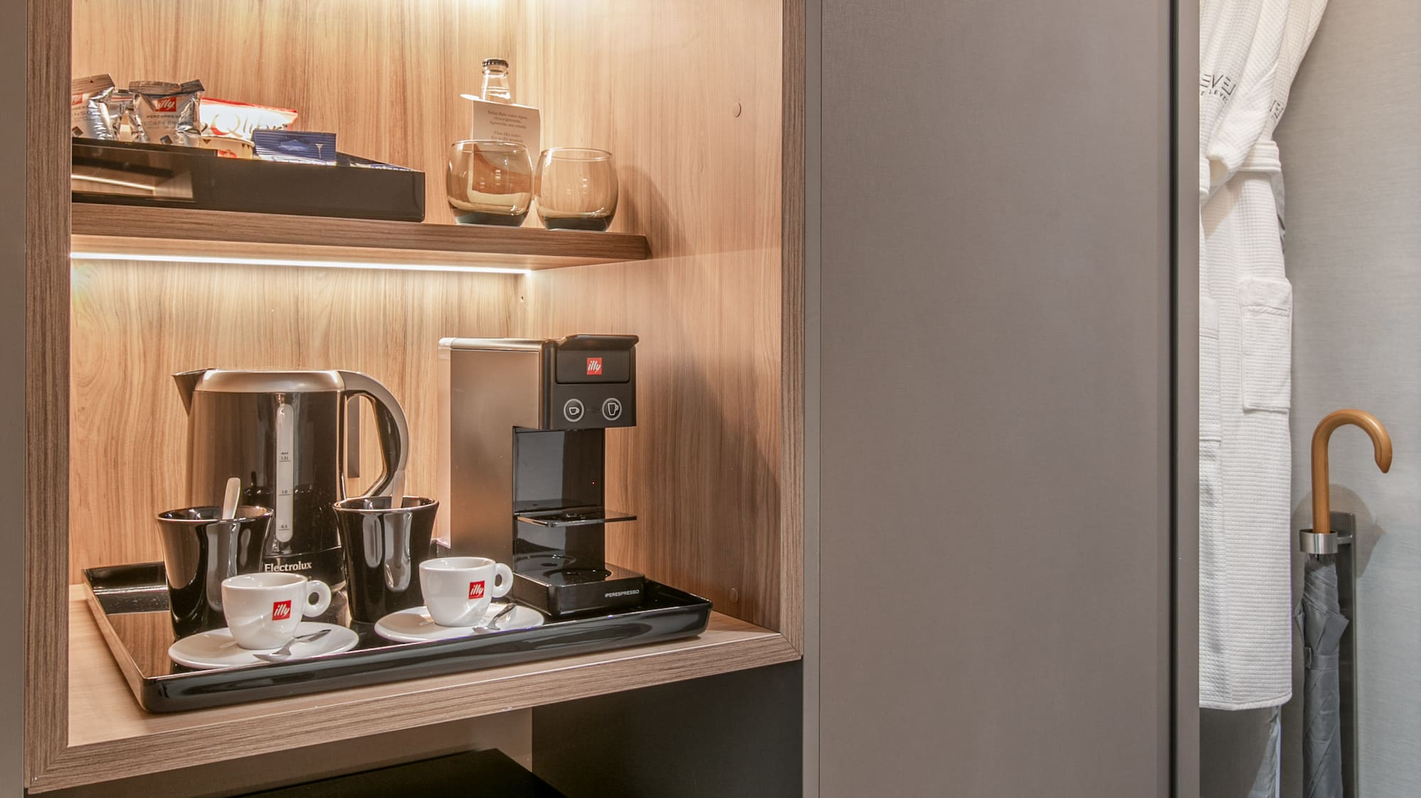 Modern hotel minibar, coffee station, and closet with illuminated shelves.