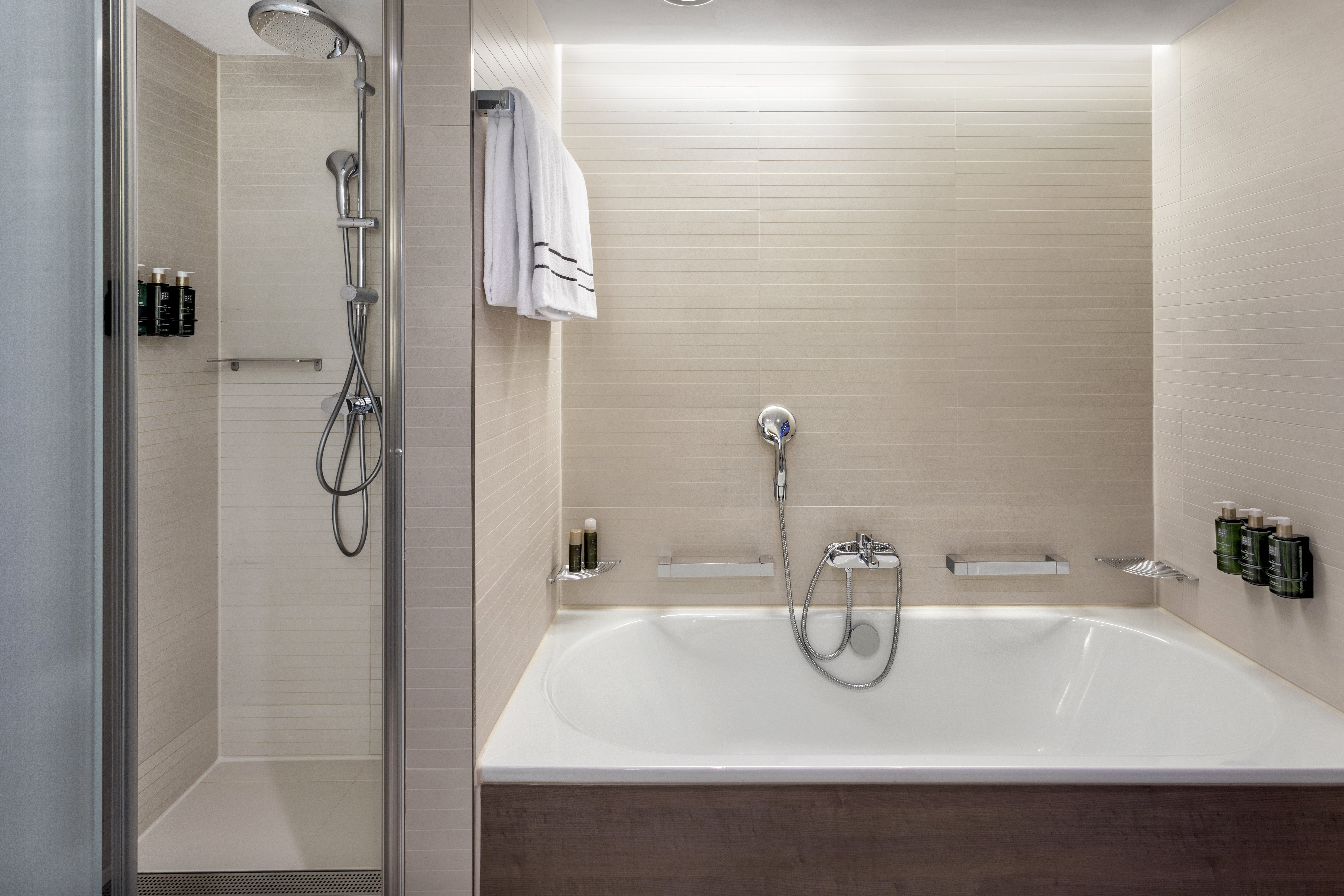 Hotel bathroom with walk-in shower, separate bathtub, and beige tiled walls.