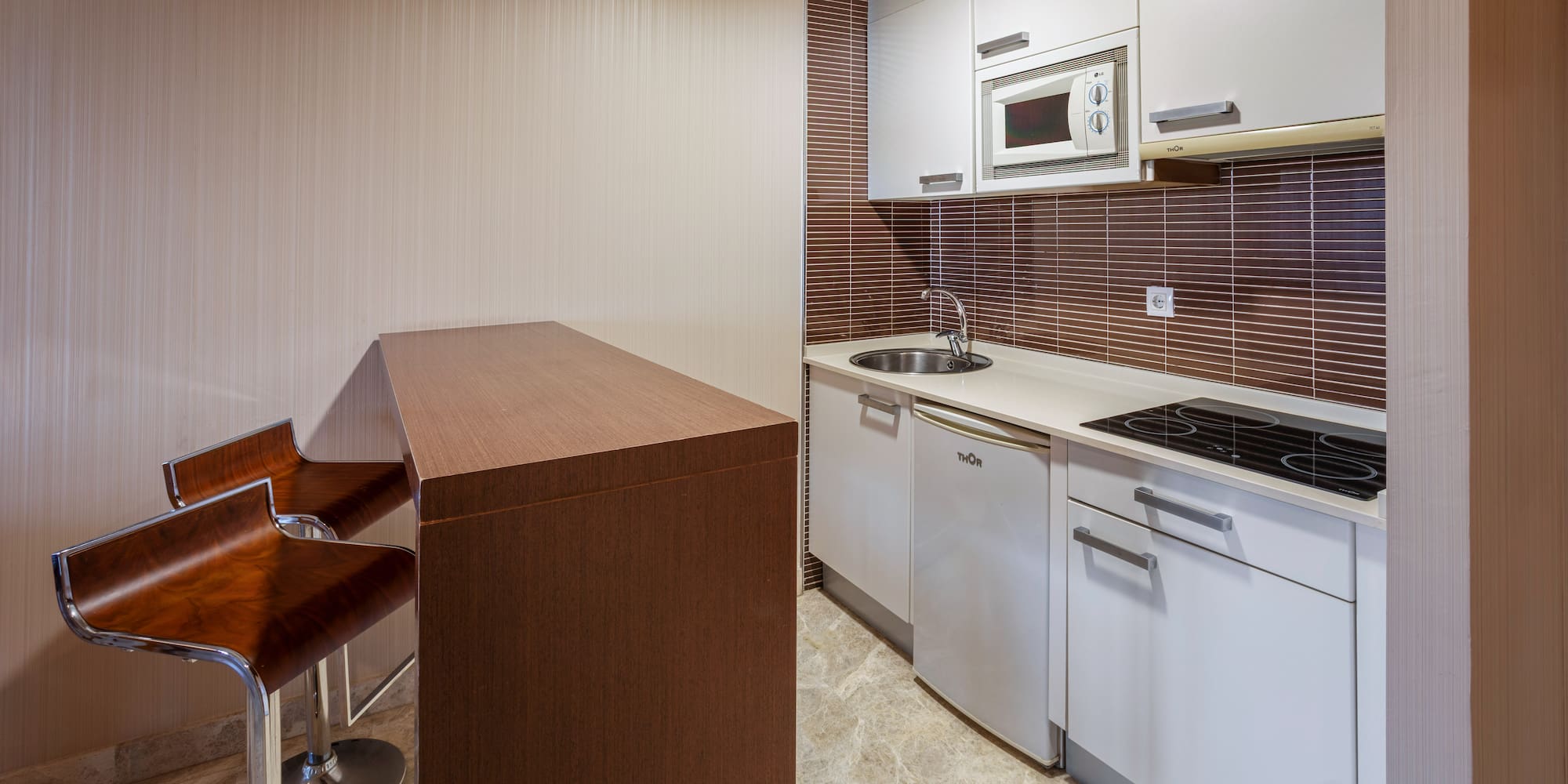 Modern kitchenette with white cabinets, breakfast bar, and bar stools.