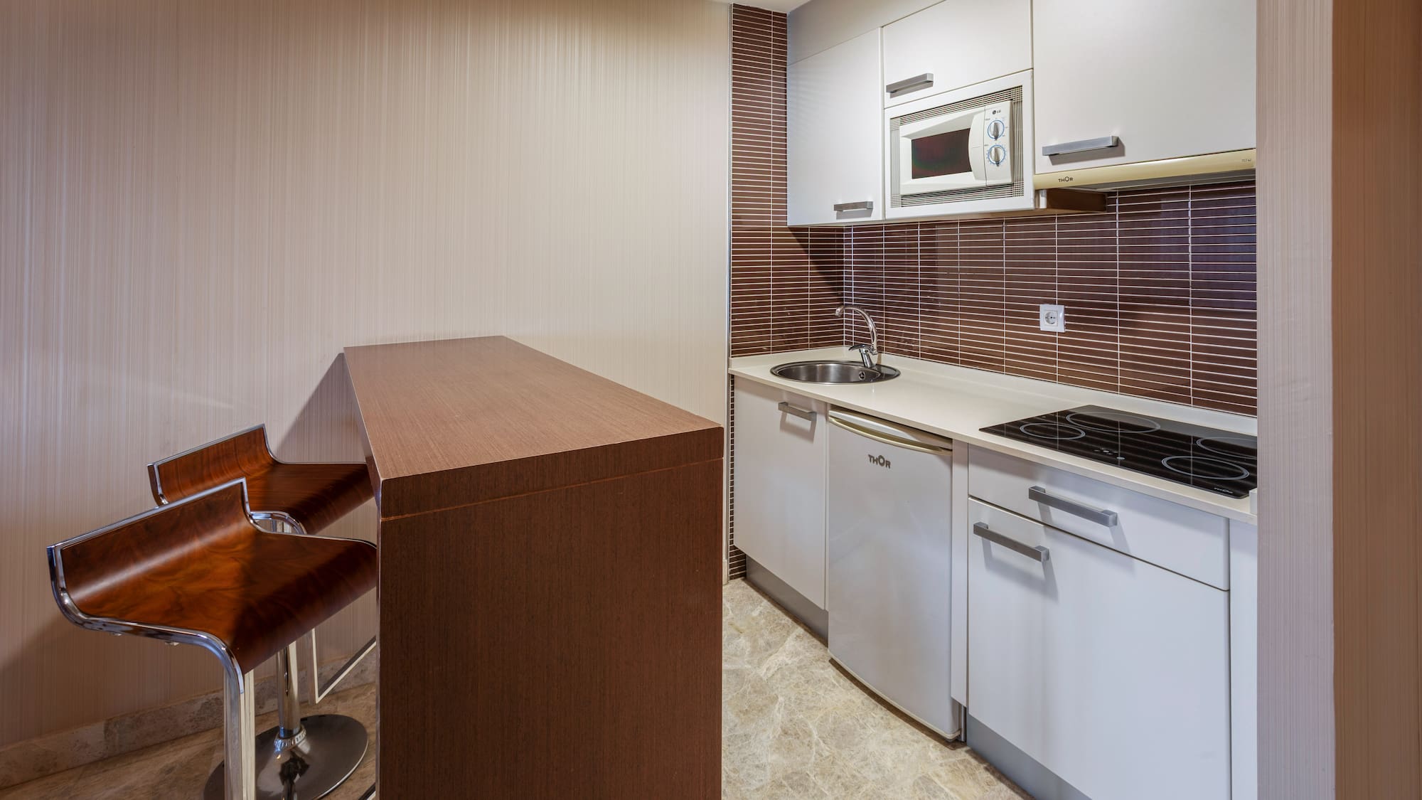 Modern kitchenette with white cabinets, breakfast bar, and bar stools.
