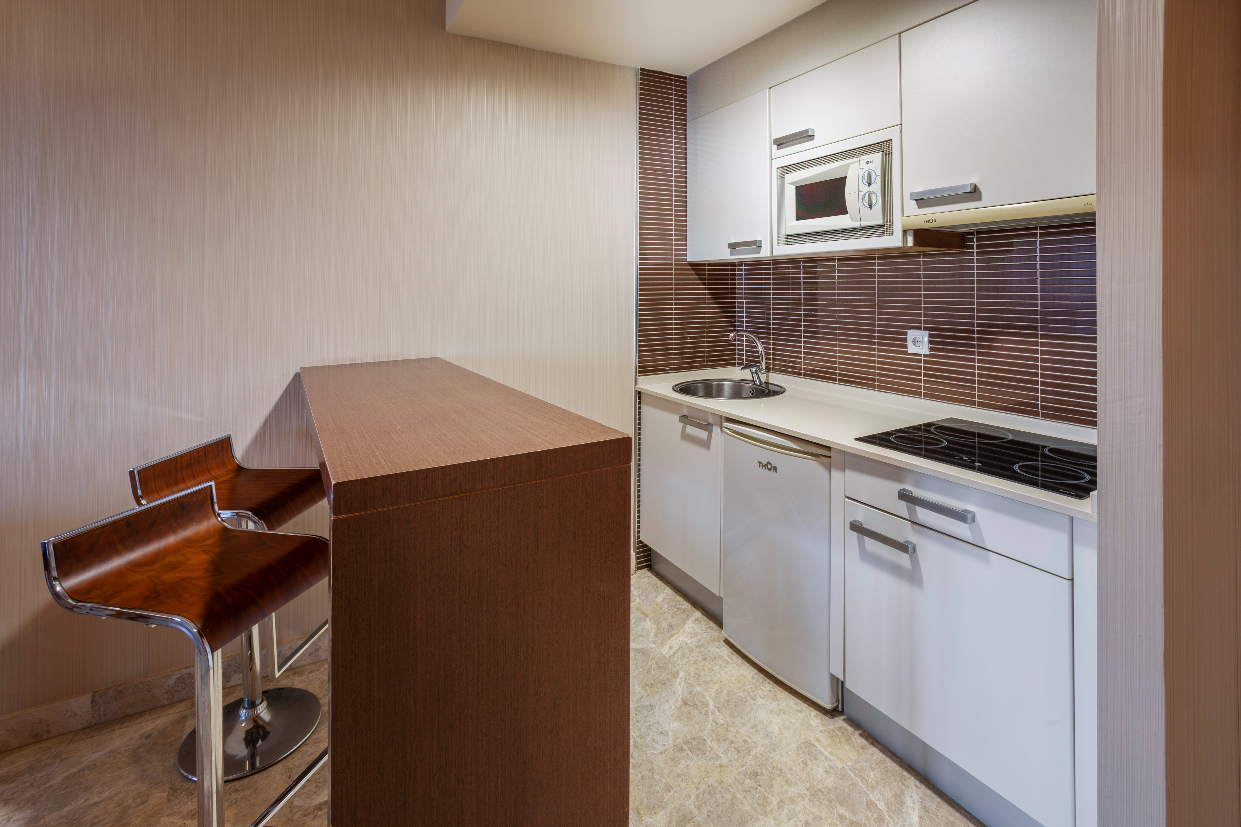 Modern kitchenette with white cabinets, brown backsplash, and breakfast bar.