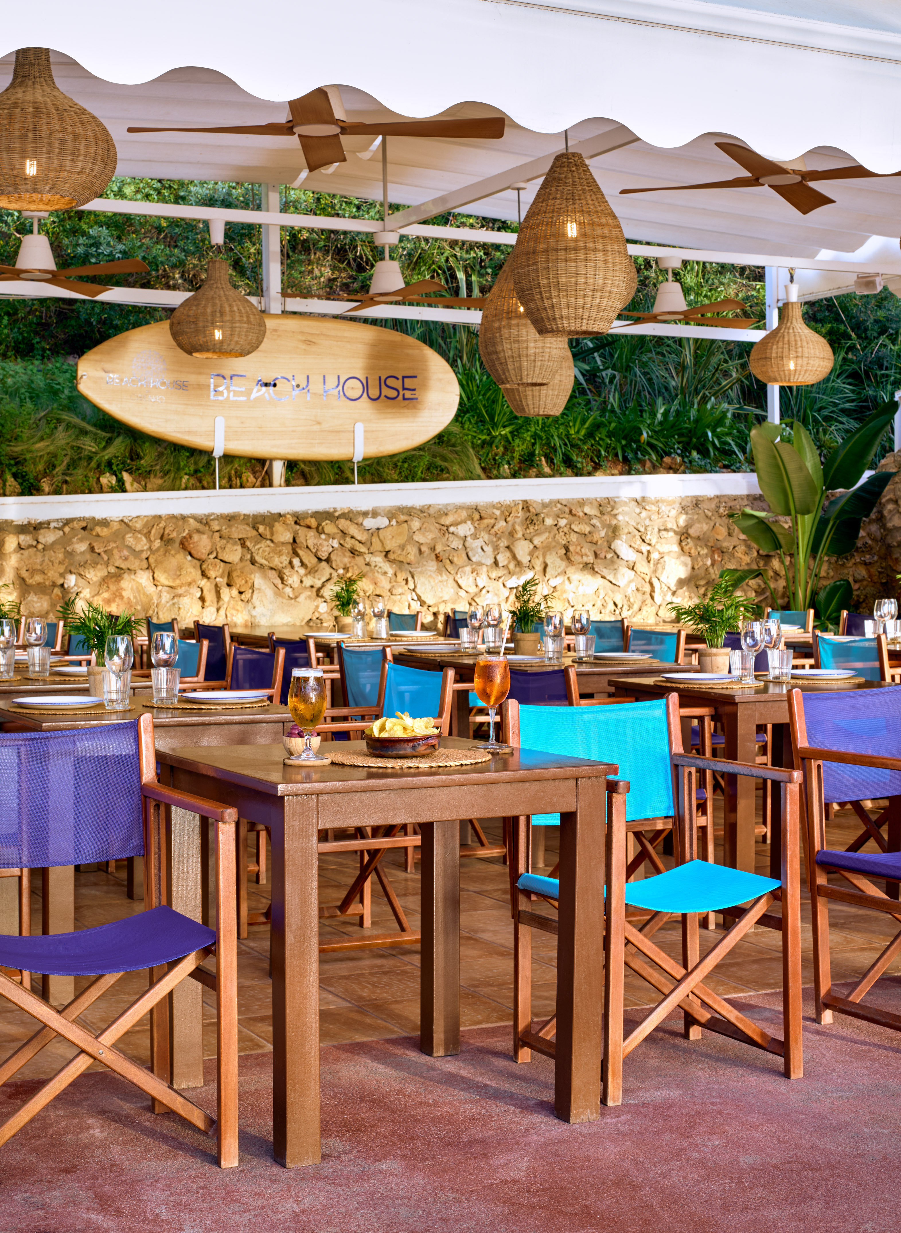 Beach House outdoor dining, blue chairs, wicker lights, tropical setting.