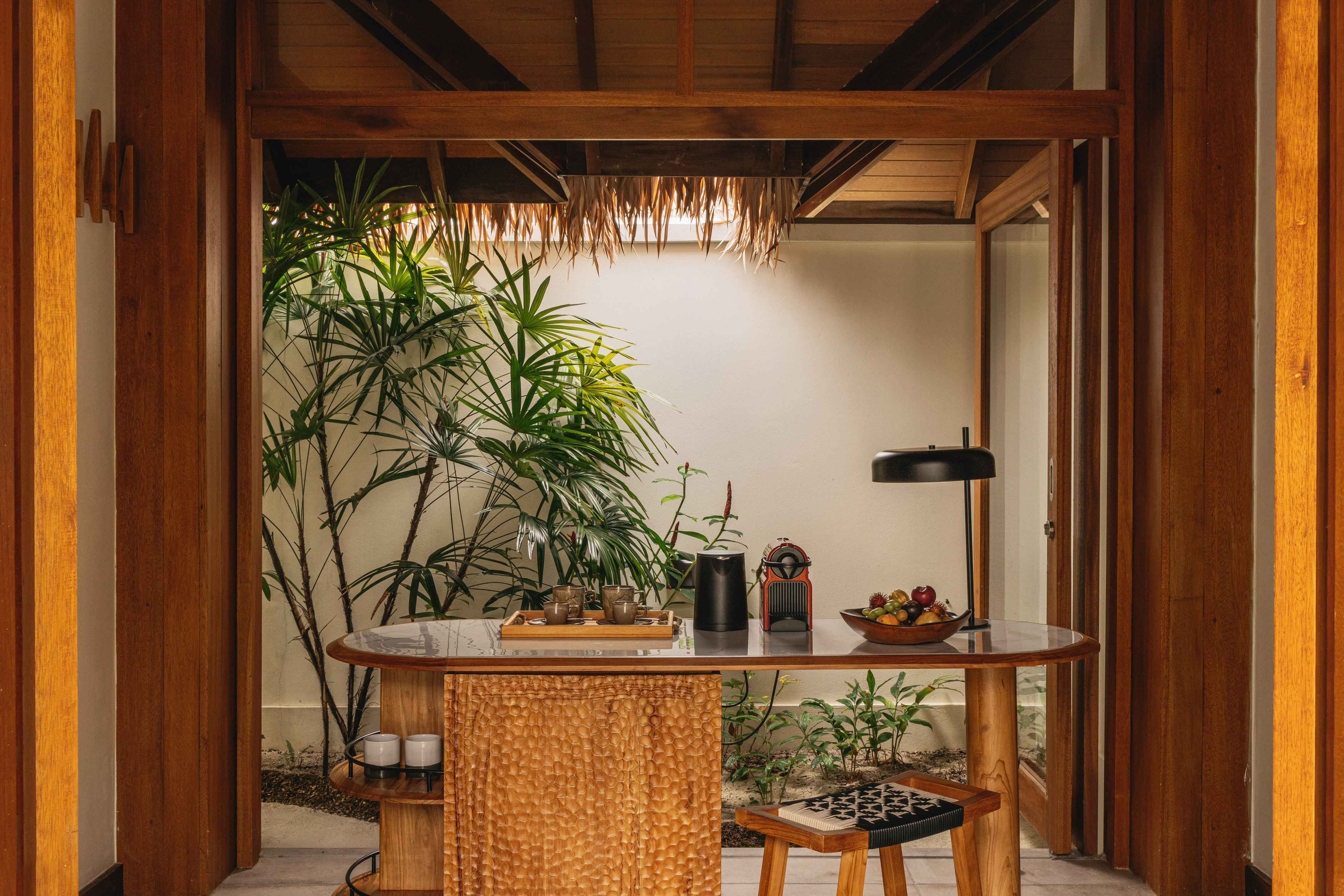 Tropical wooden minibar with Nespresso machine, fruit, and lush plants.
