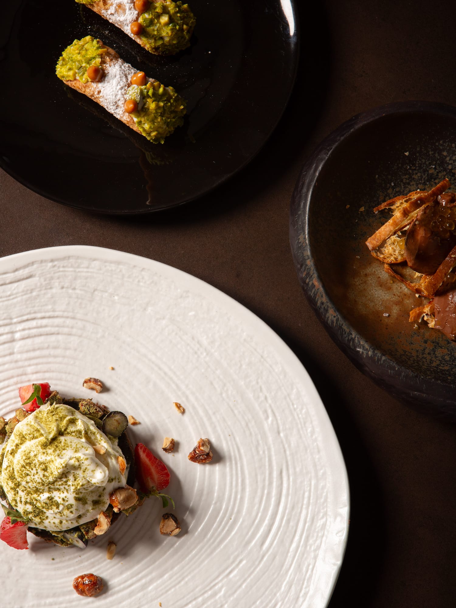 Pistachio cannoli and gourmet matcha dessert with berries and nuts on styled plates.