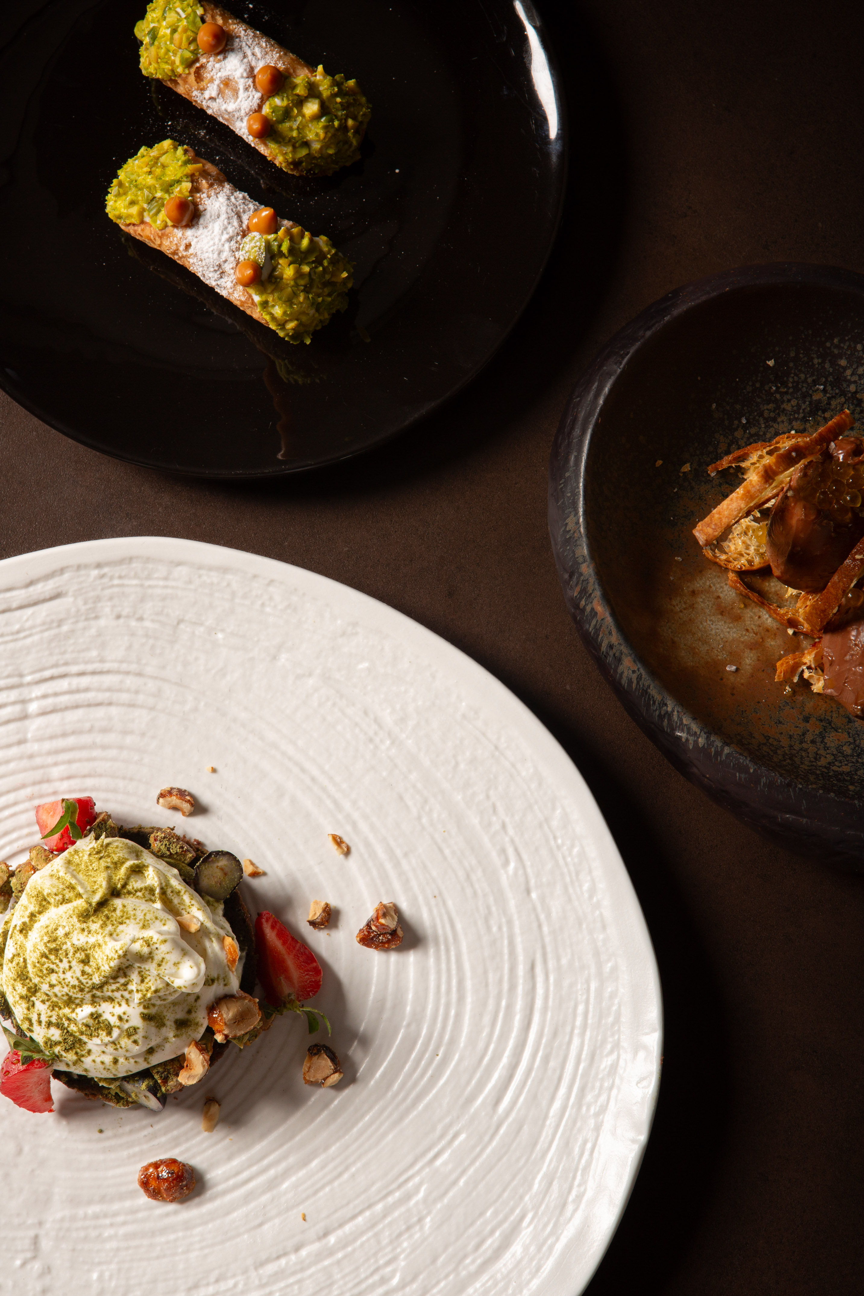 Pistachio cannoli and gourmet matcha dessert with berries and nuts on styled plates.