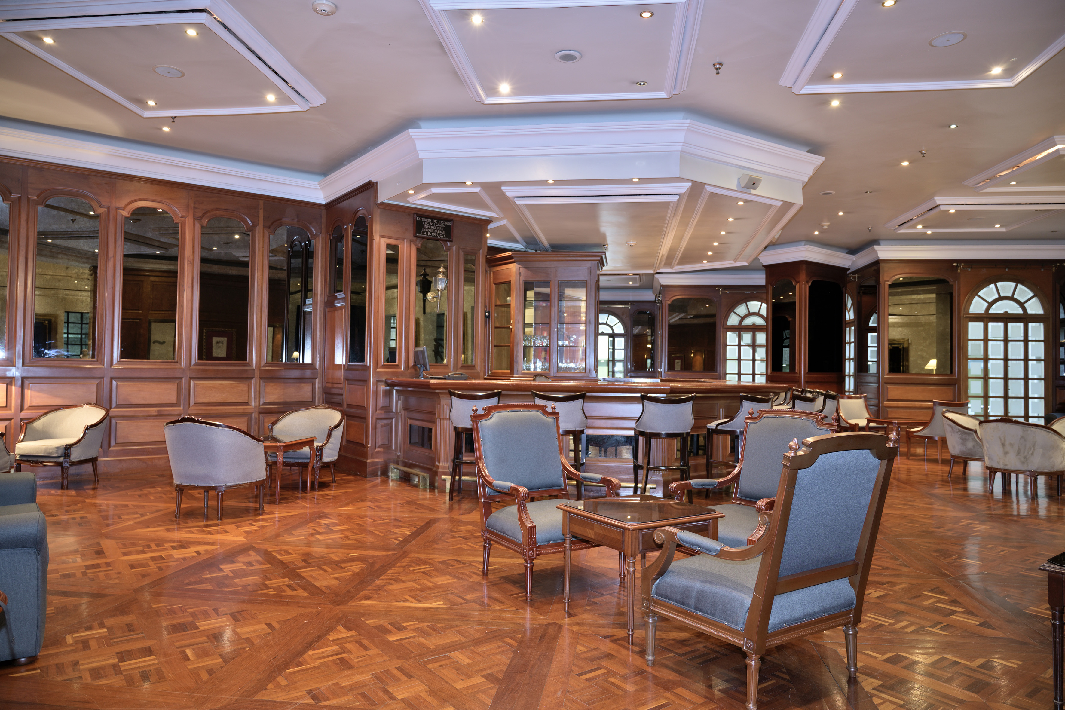 Elegant hotel bar lounge, rich wood interior, parquet floor, plush chairs.
