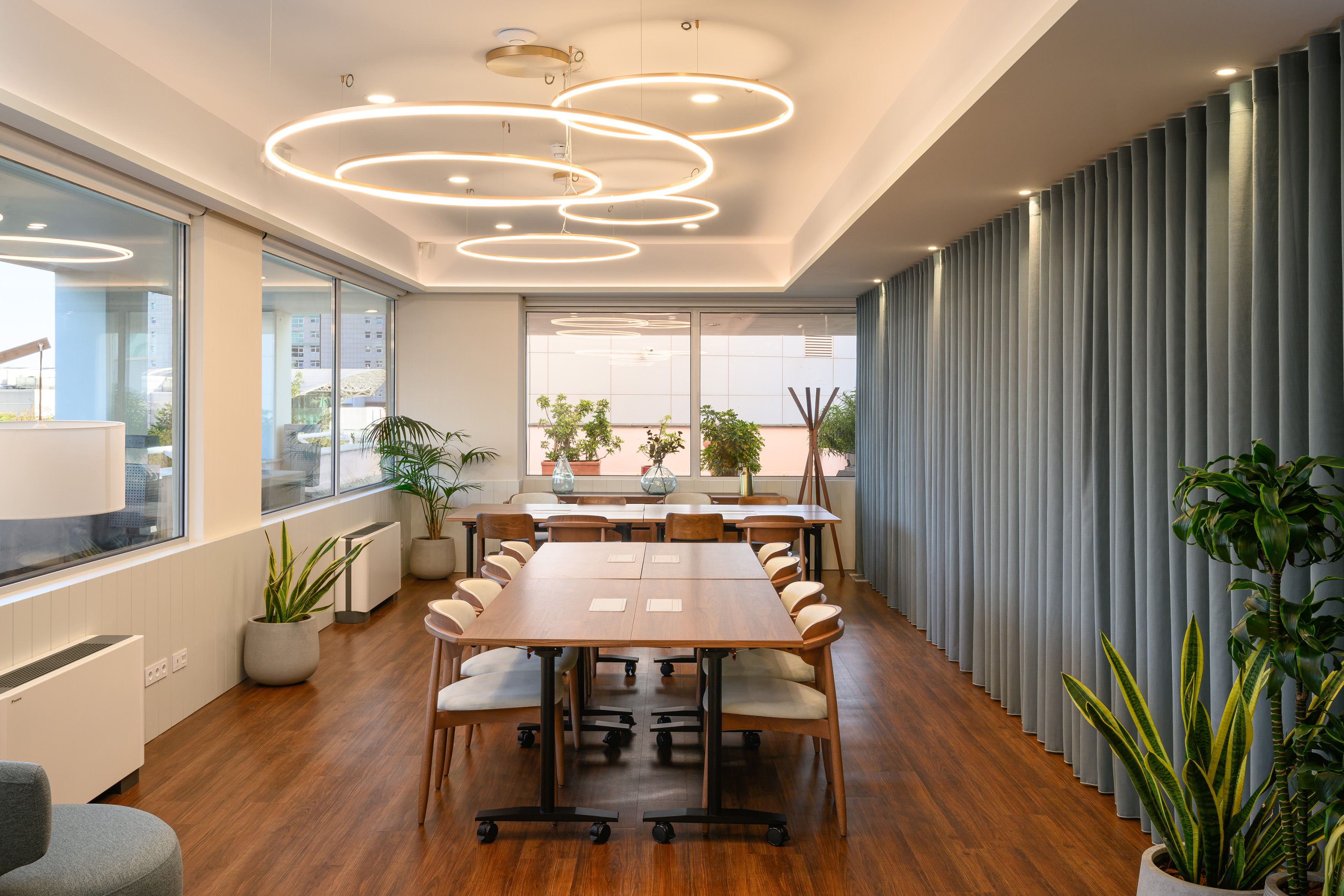 Modern meeting room with large wooden tables, circular LED lights, and plants.