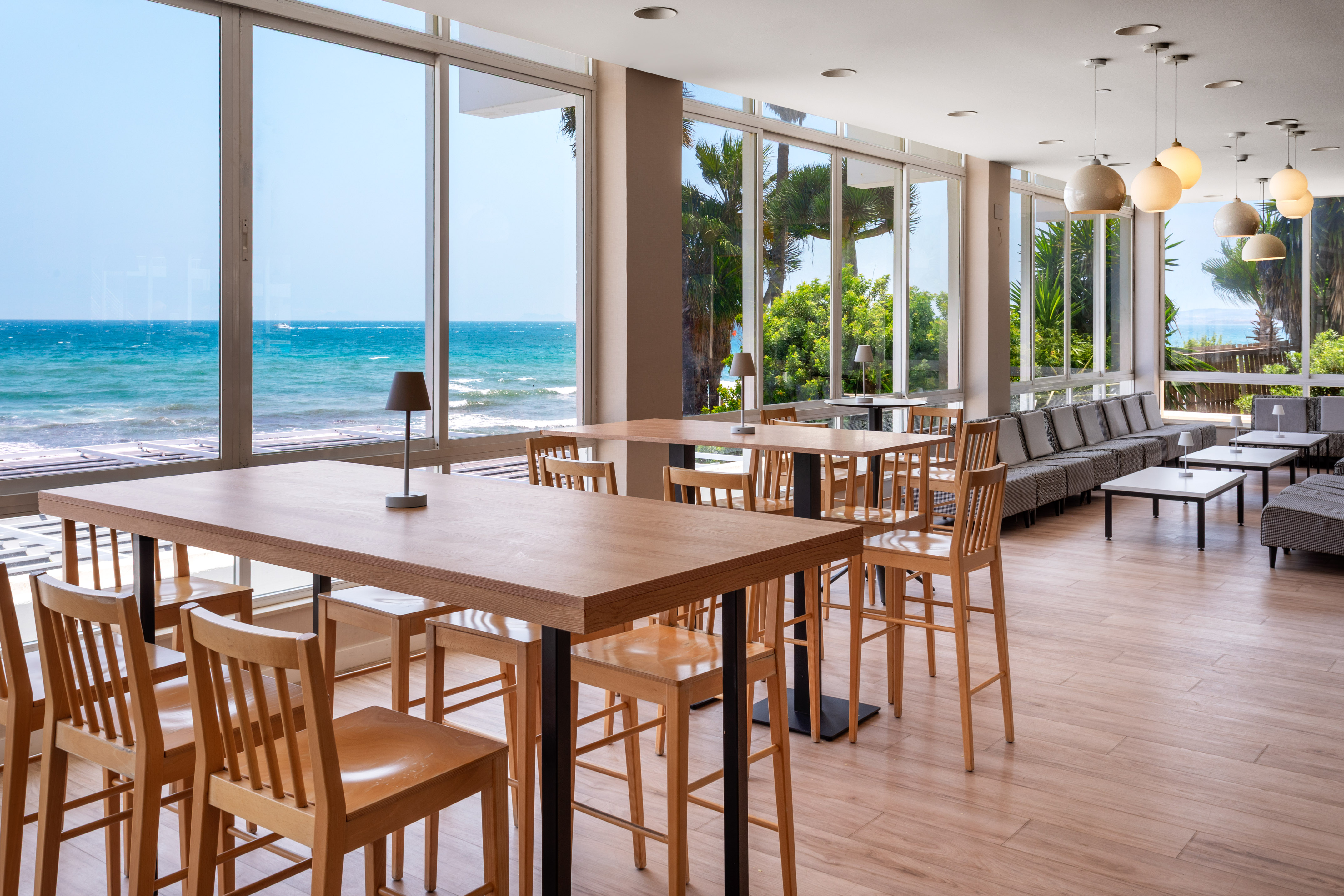 Modern seaside lounge with ocean view, high wooden tables, and comfortable sofas.