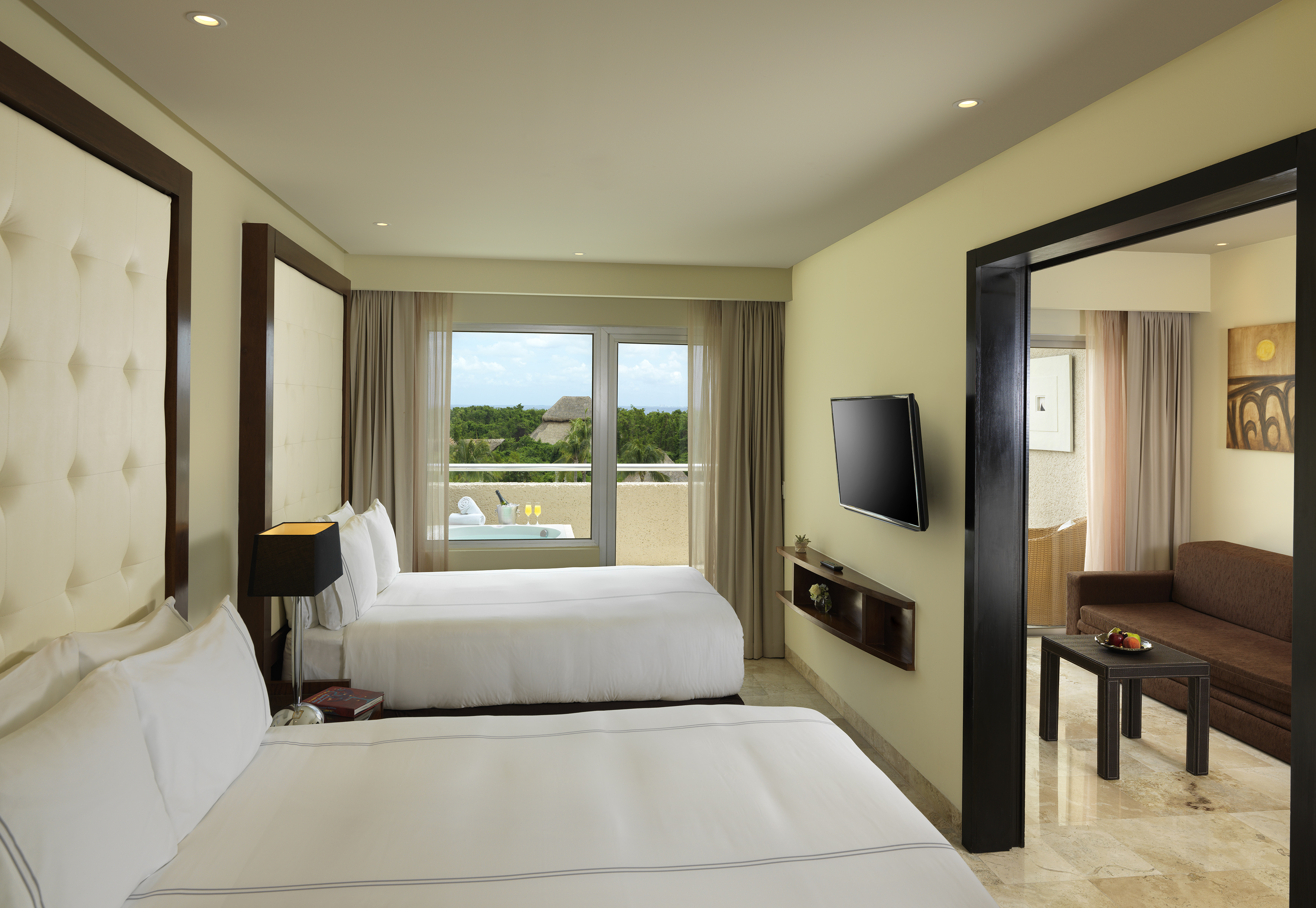 Hotel suite with two beds, private balcony hot tub, and tropical view.