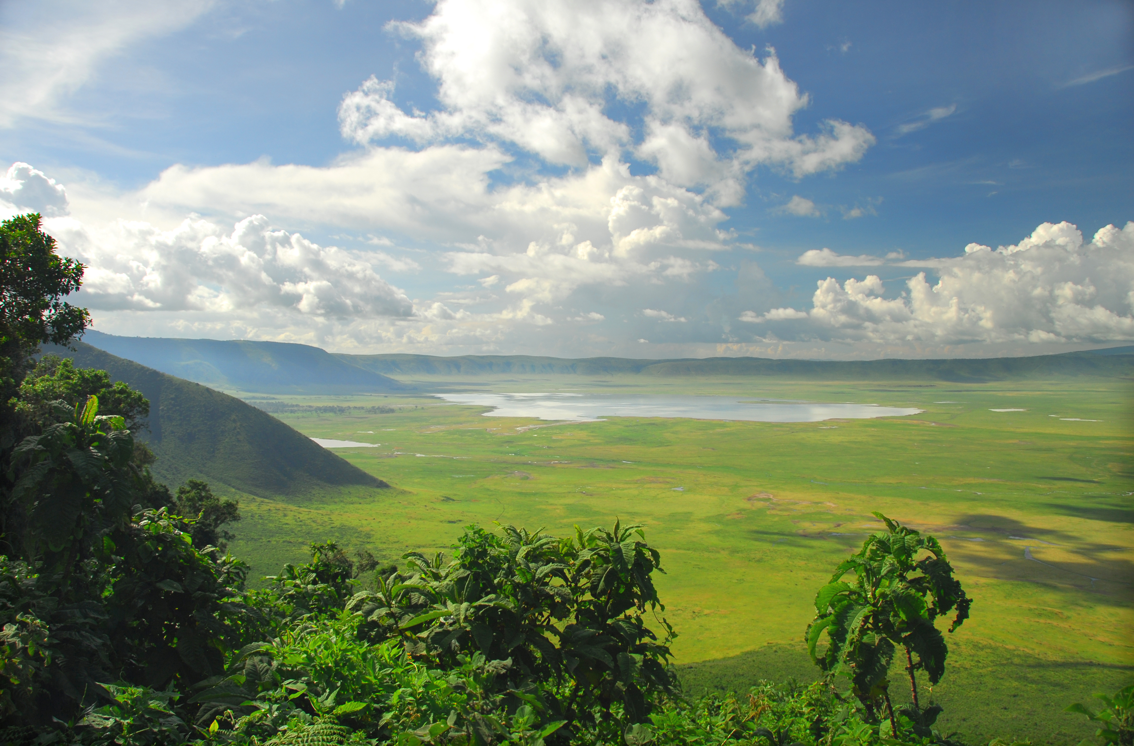 Ngorongoro Crater vista: vast green plains, central lake, mountains, blue sky.