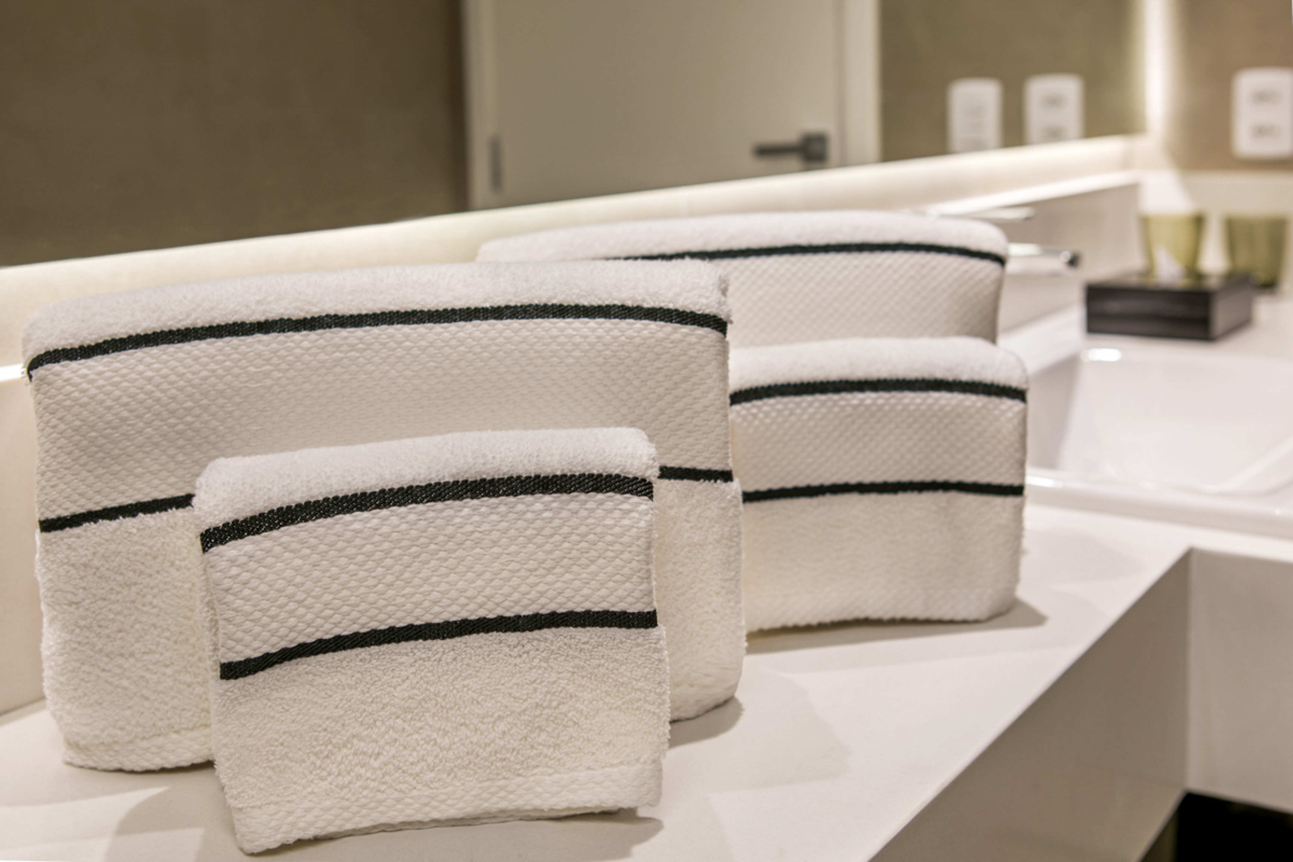 Stack of white towels with black stripes in a hotel bathroom.