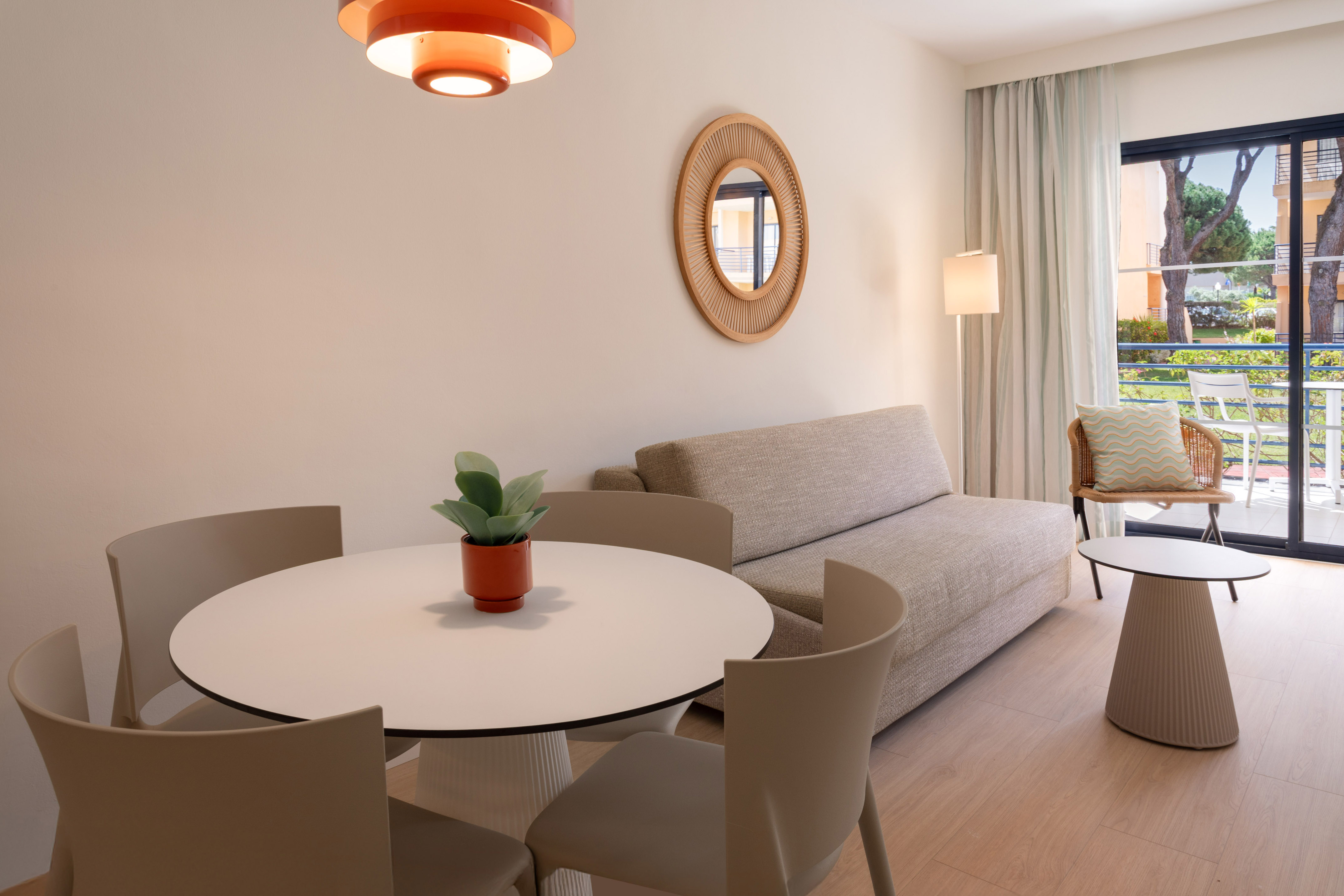 Bright hotel apartment with dining table, sofa, and balcony access.