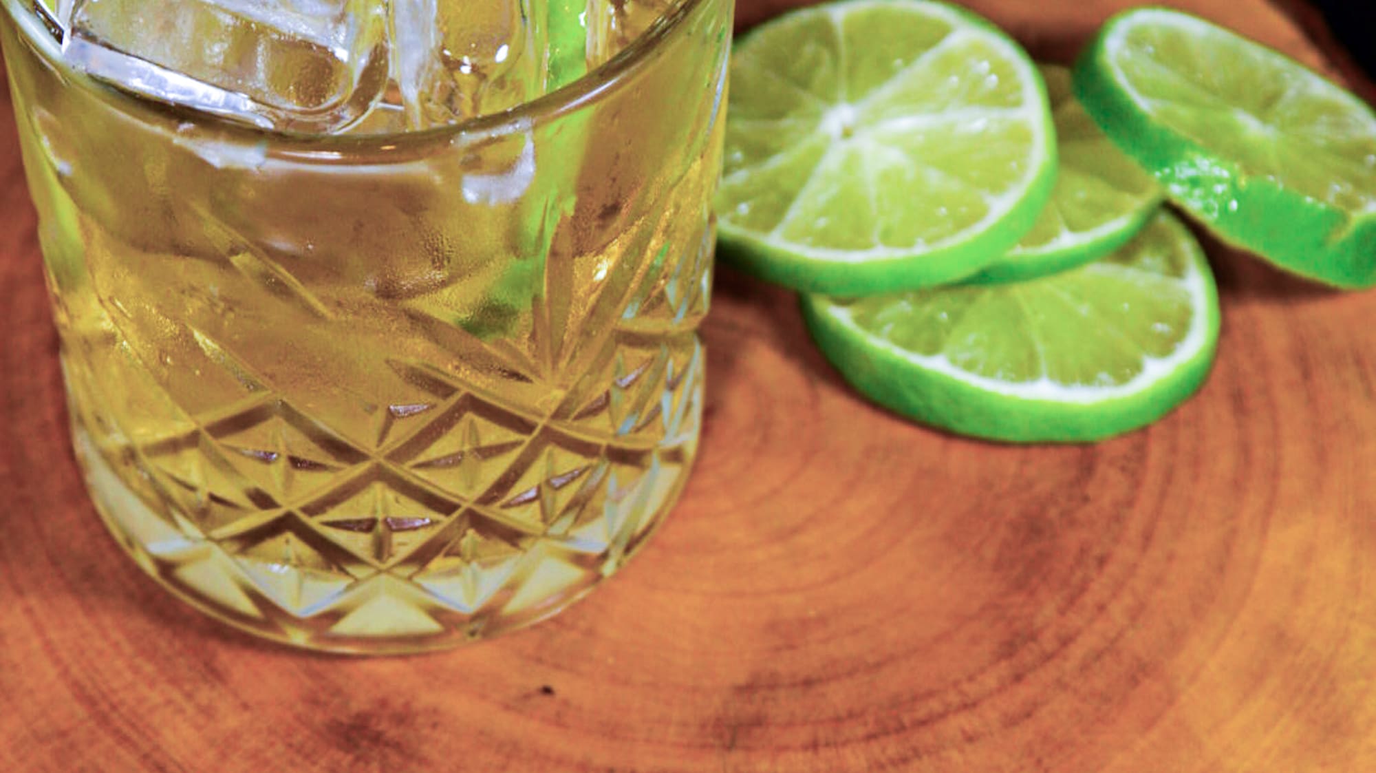 a glass of ice and limes on a wood surface
