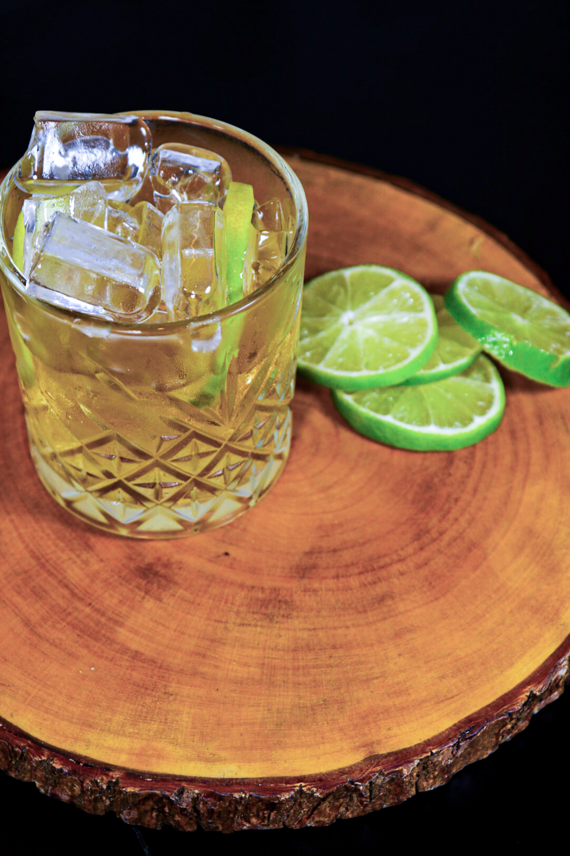 Whiskey cocktail with ice and lime slices on a wood board.