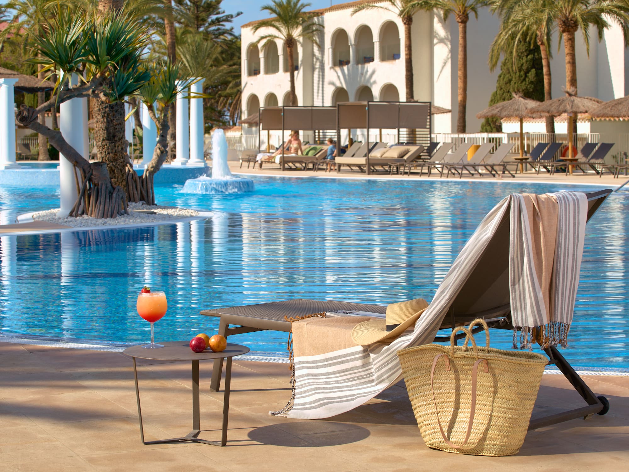 Lounge chair, cocktail by a sunny resort swimming pool with palm trees.