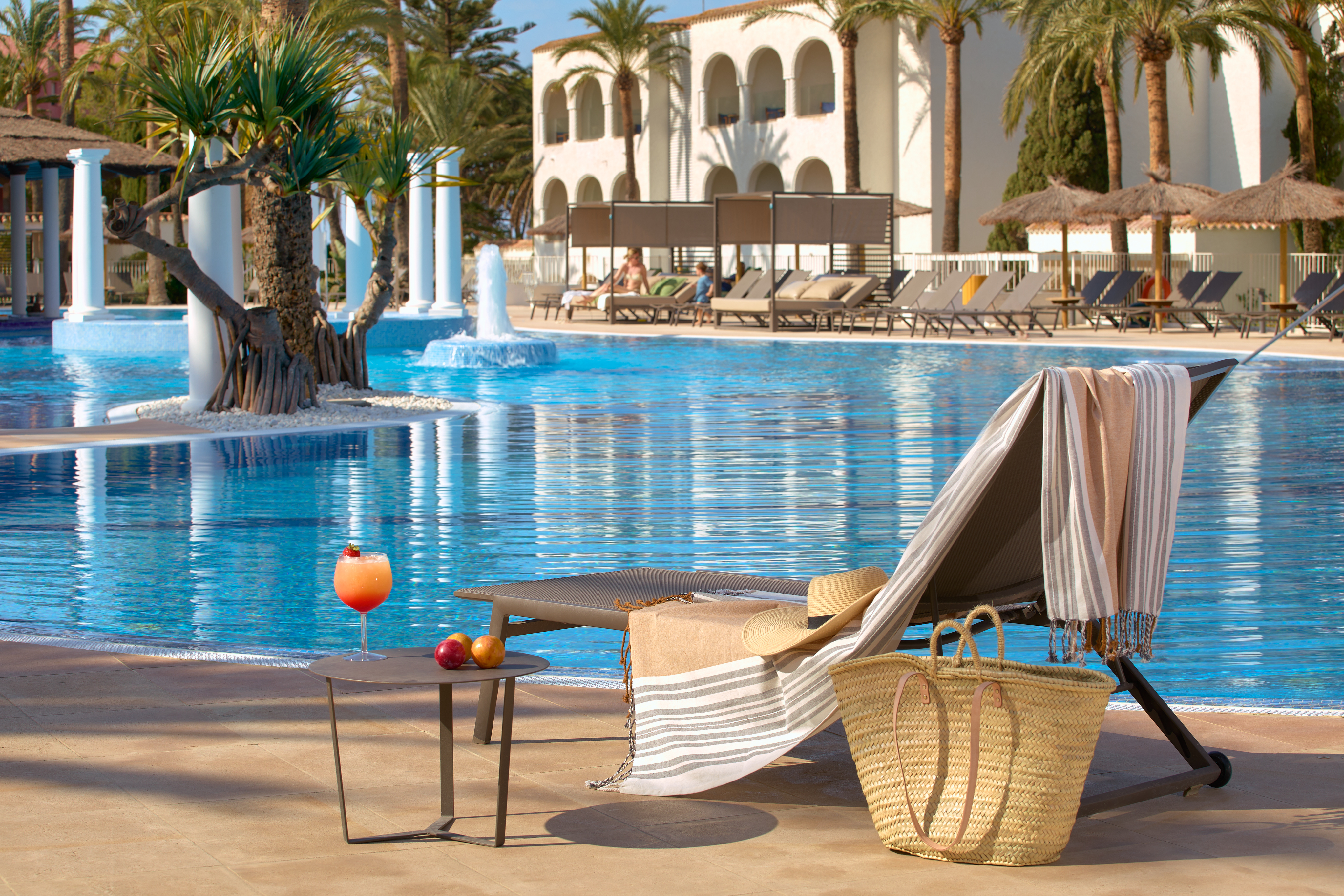 Lounge chair, cocktail by a sunny resort swimming pool with palm trees.