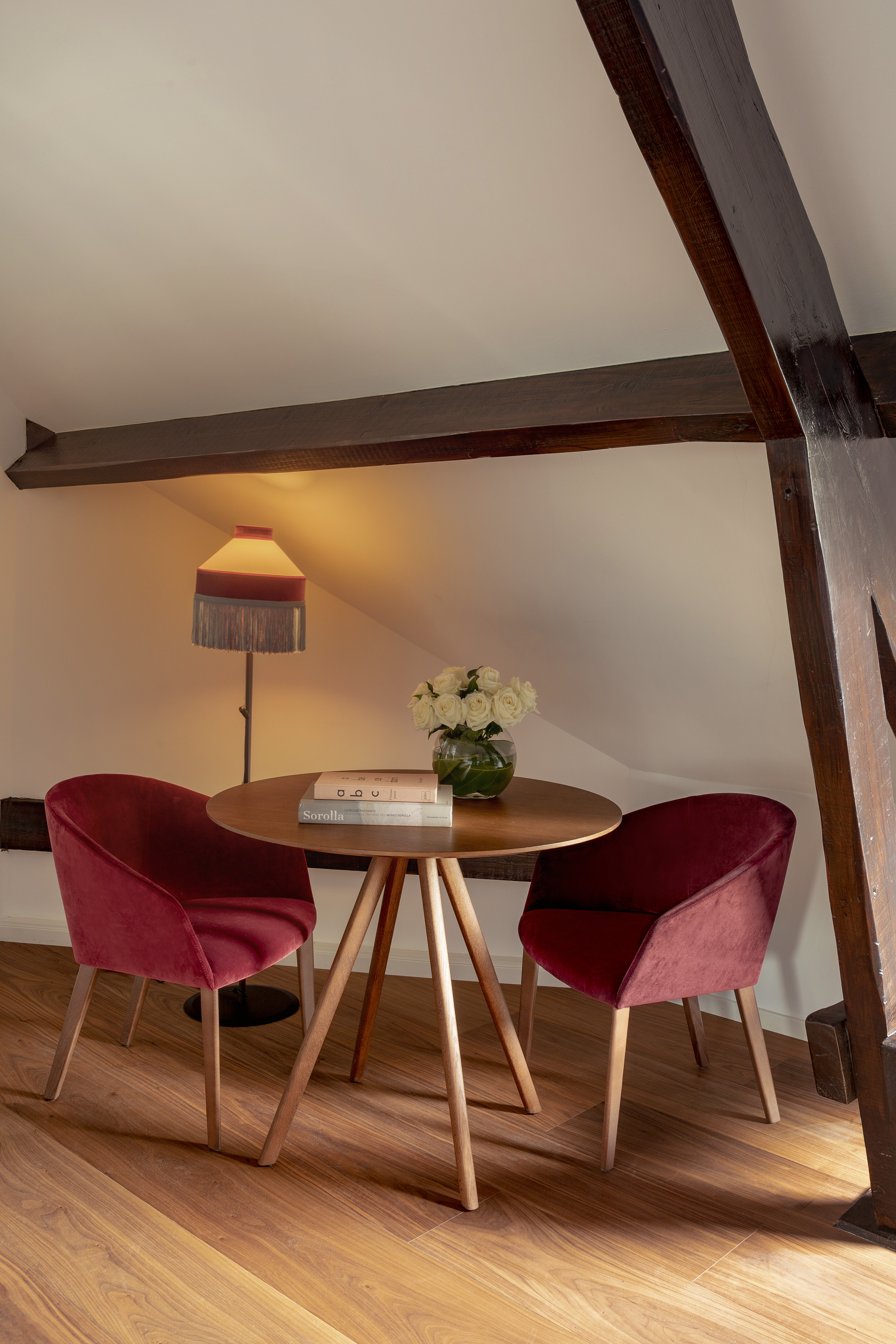 Red velvet chairs, wooden table, and exposed beams in cozy attic room.