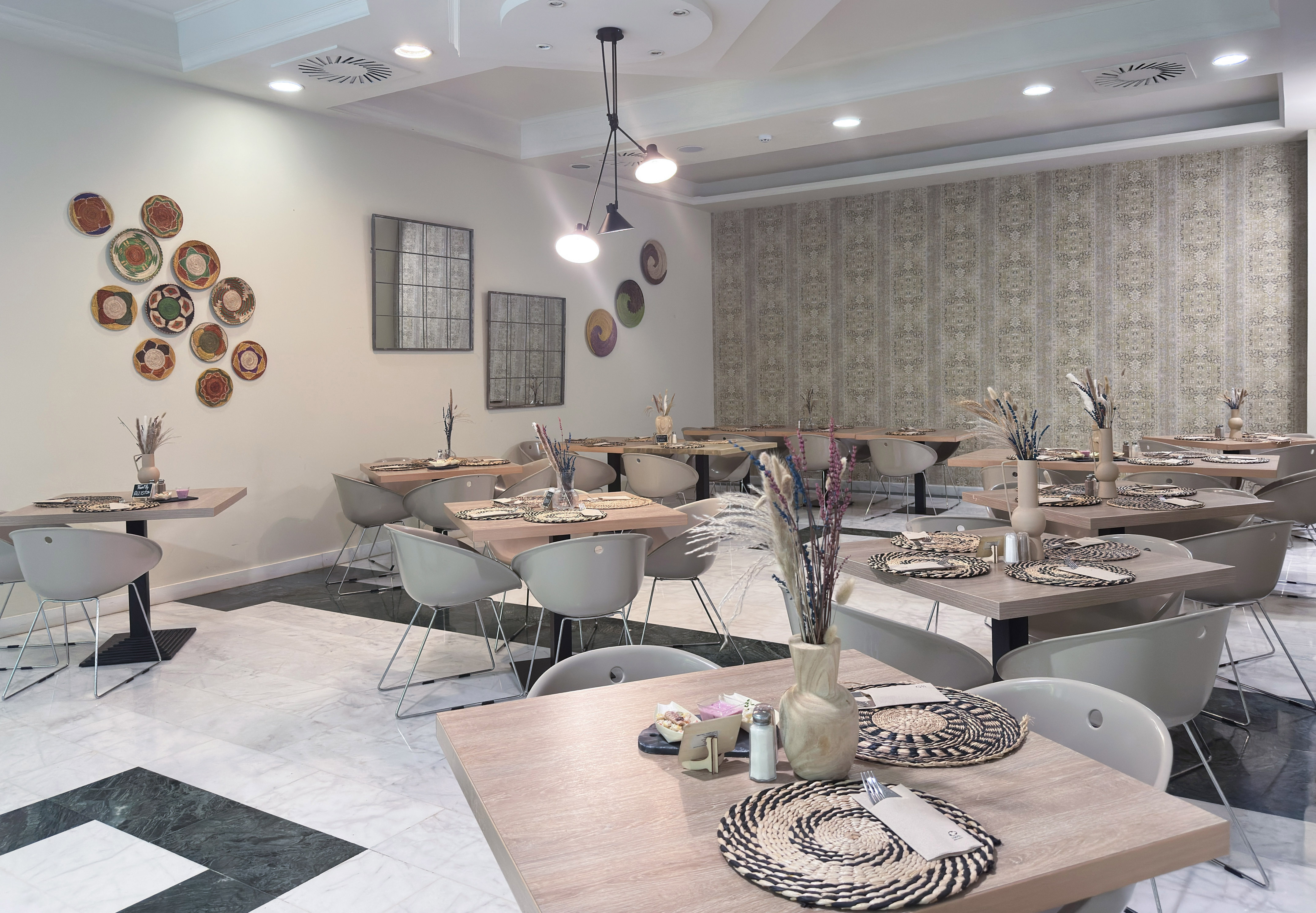 Modern restaurant dining room with light wood tables, grey chairs, and patterned walls.