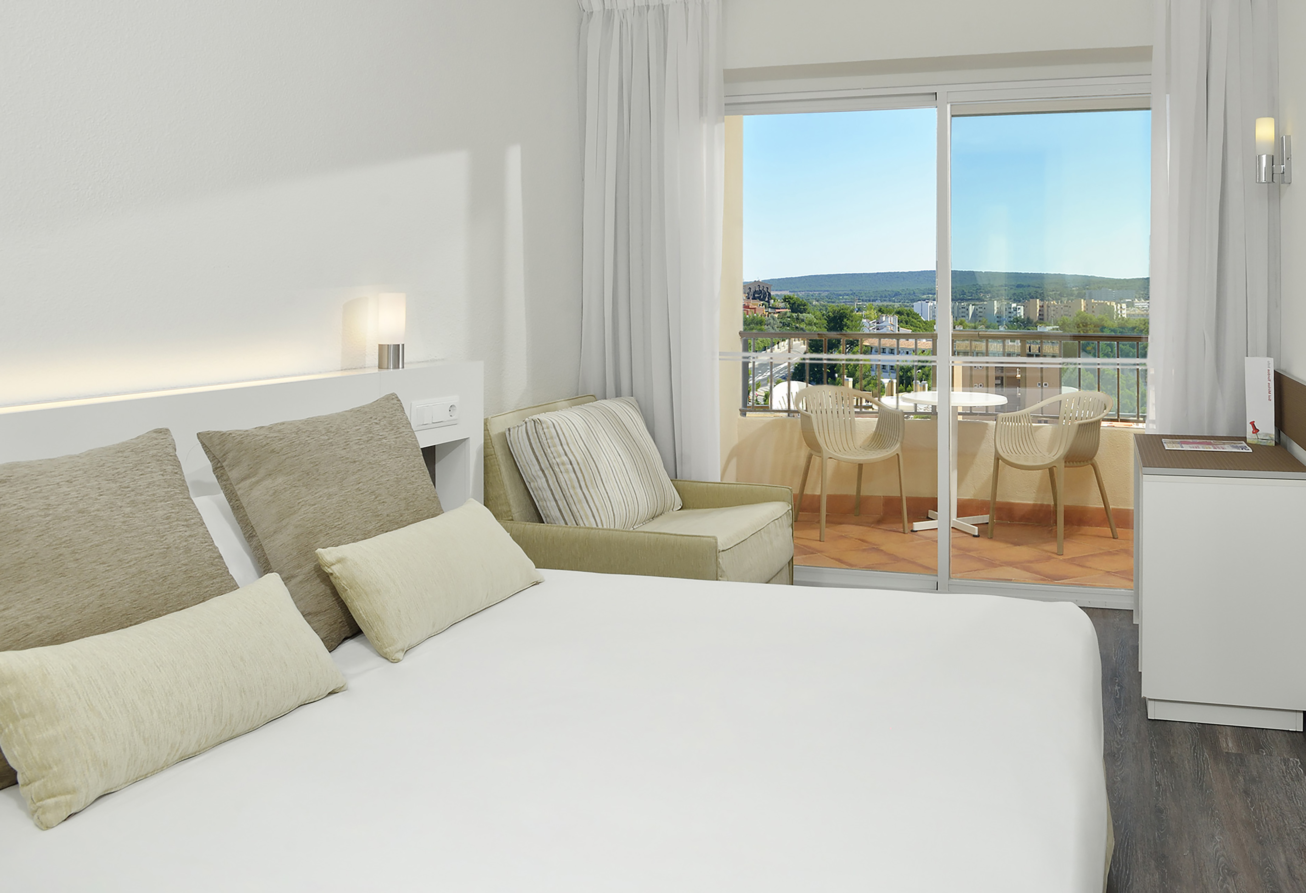 Modern hotel bedroom with white bed, private balcony, and scenic town view.